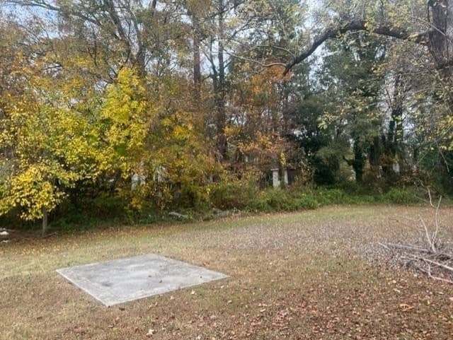 A concrete slab sits in the foreground of a landscape with leafy trees exhibiting autumn colors, and a grassy area that slightly extends towards a wooded backdrop.