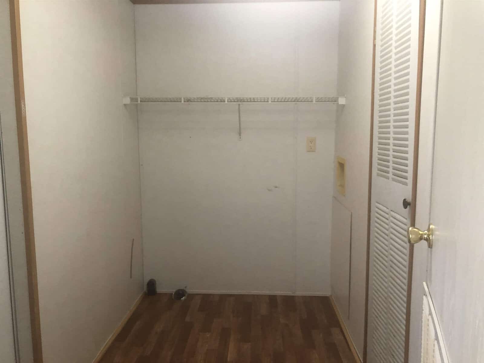 An empty room with white walls, a wooden floor, and a single shelf mounted near the ceiling.