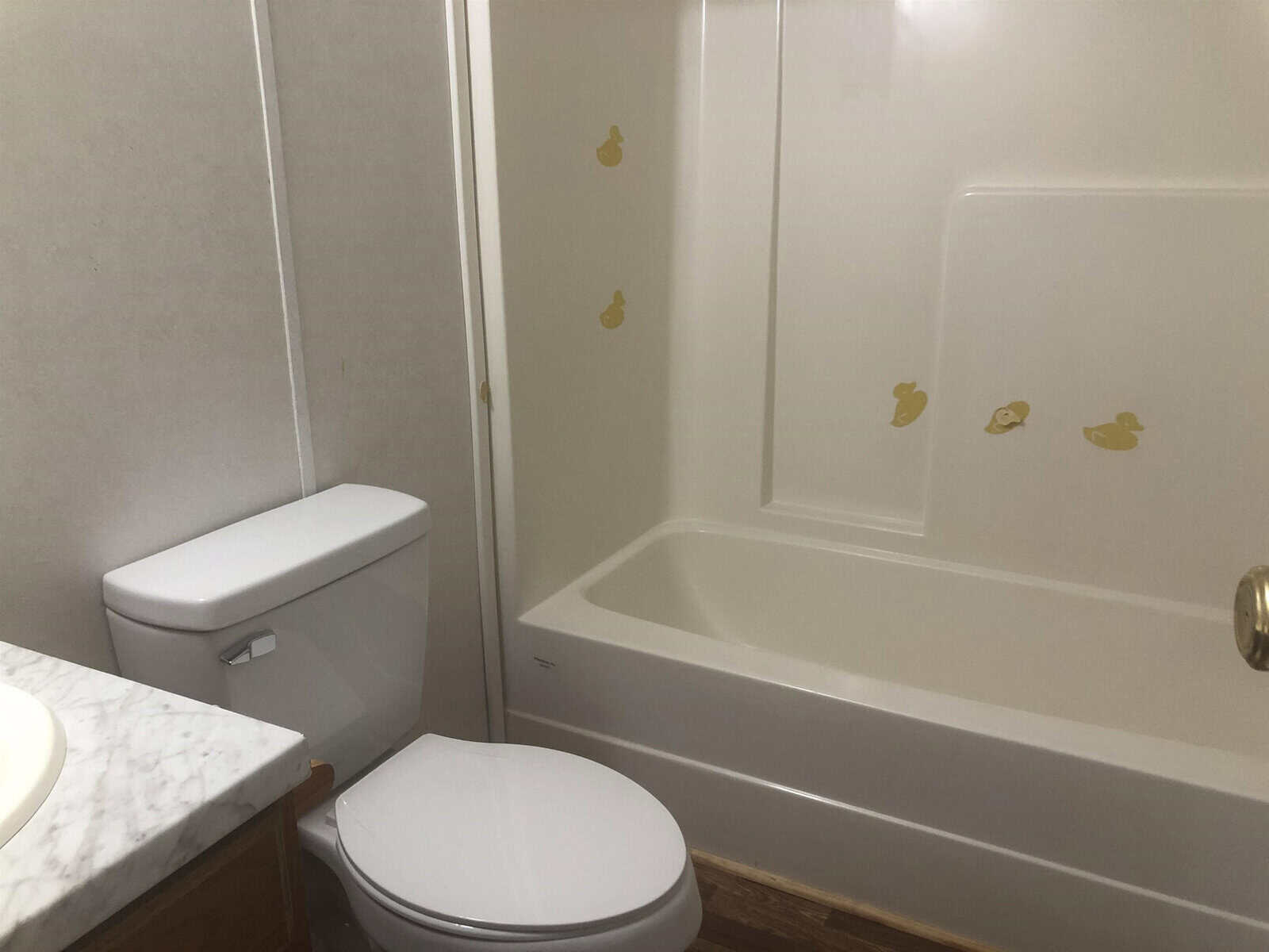A bathroom interior featuring a white toilet next to a vanity and a bathtub with a few decorative decals on the wall.