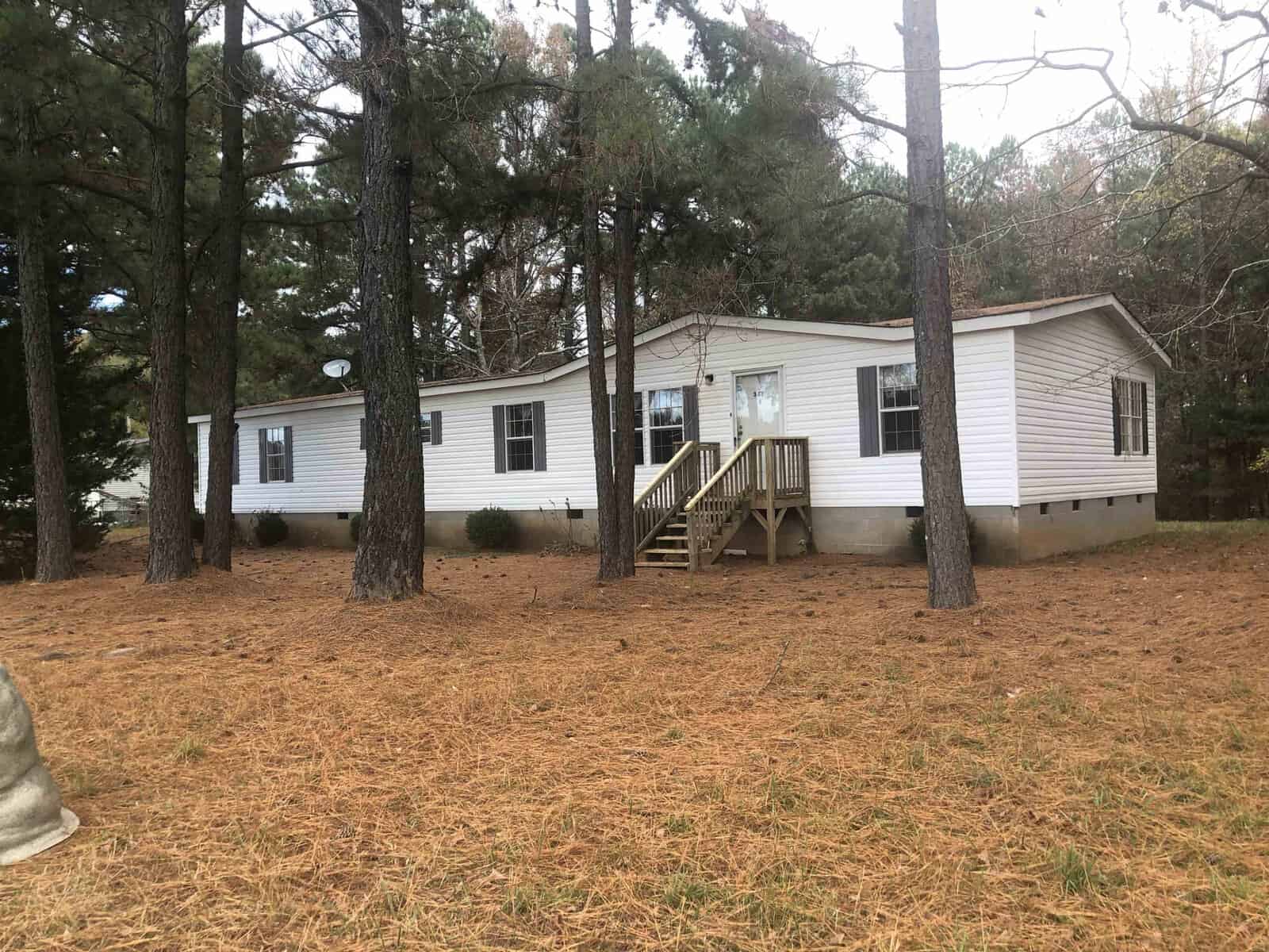 A single-story mobile home with white siding, located at 341 Tower Lane, Henderson NC, in a wooded area with a front staircase leading to the entrance, surrounded by a yard with pine needles.