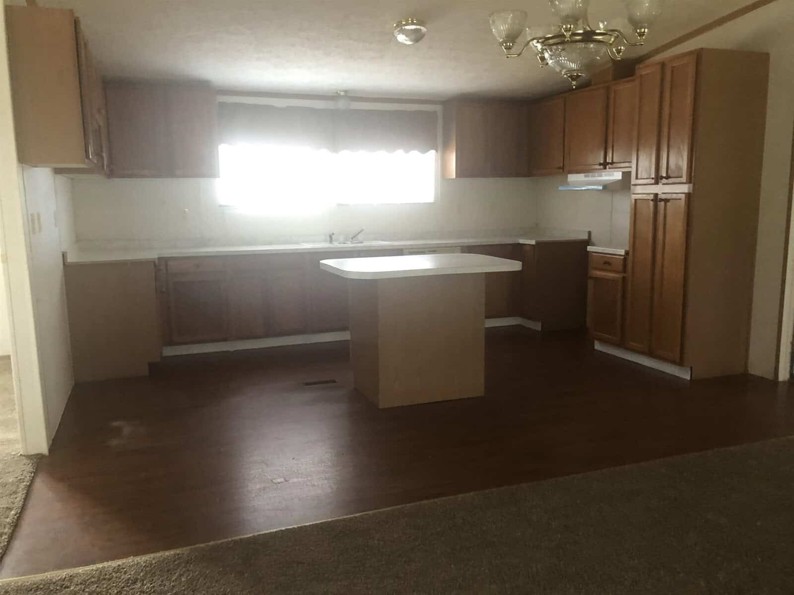 An empty kitchen with brown wooden cabinets, a white countertop, and dark flooring.