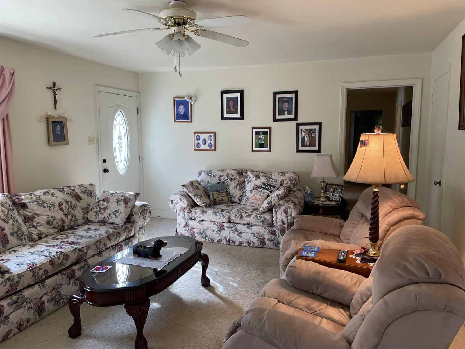 A traditionally furnished living room with floral patterned sofas, a wooden coffee table, and walls decorated with framed photographs.