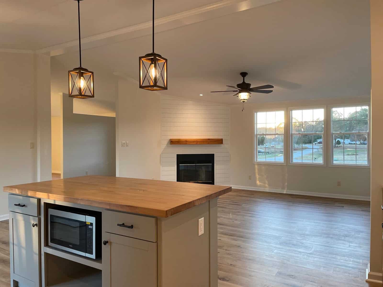 A spacious, modern kitchen with pendant lighting, a central island, and a fireplace, opening into a living area with natural light from large windows.