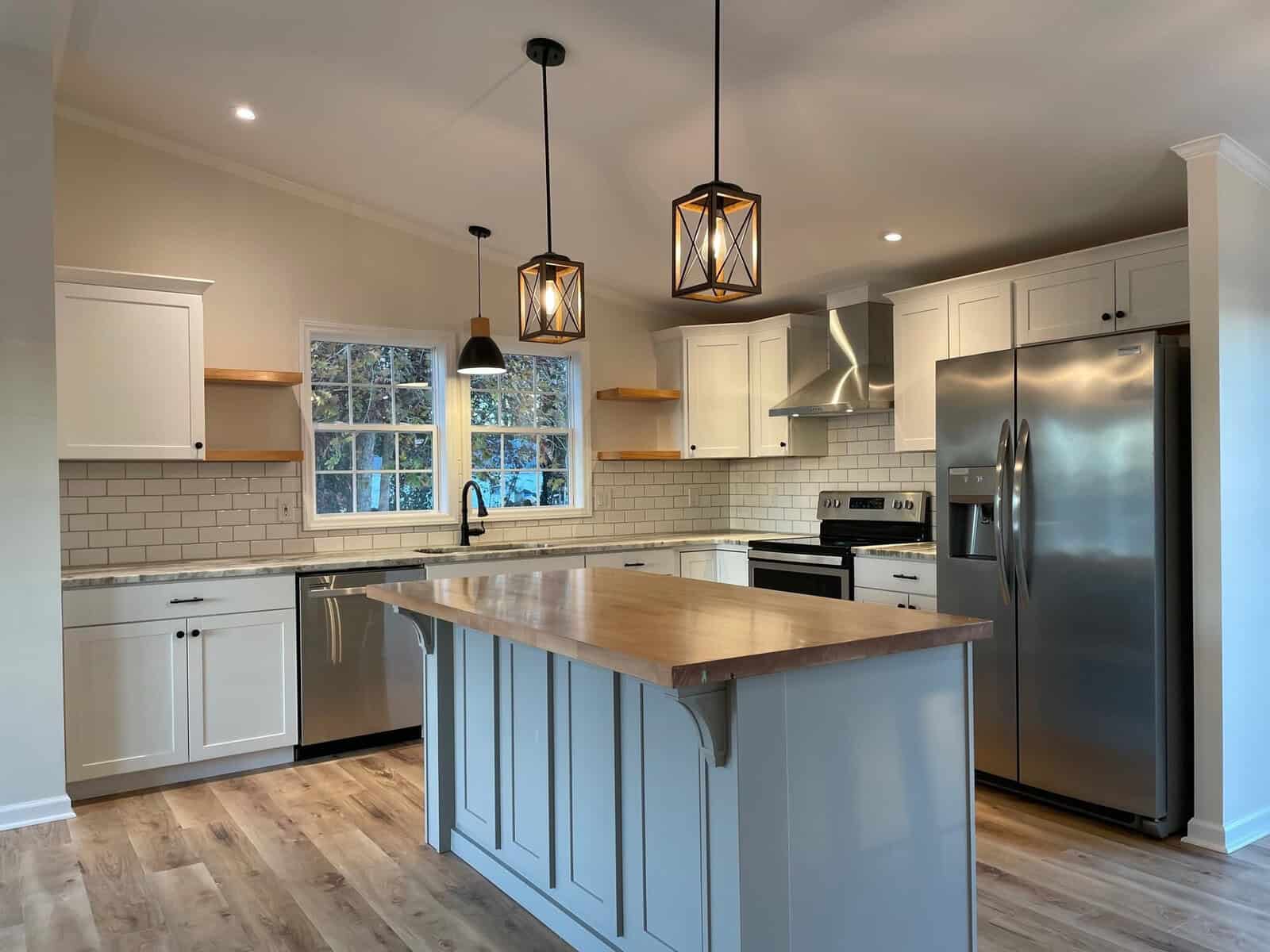 A modern kitchen interior with white cabinetry, stainless steel appliances, pendant lighting, and a wooden countertop island.