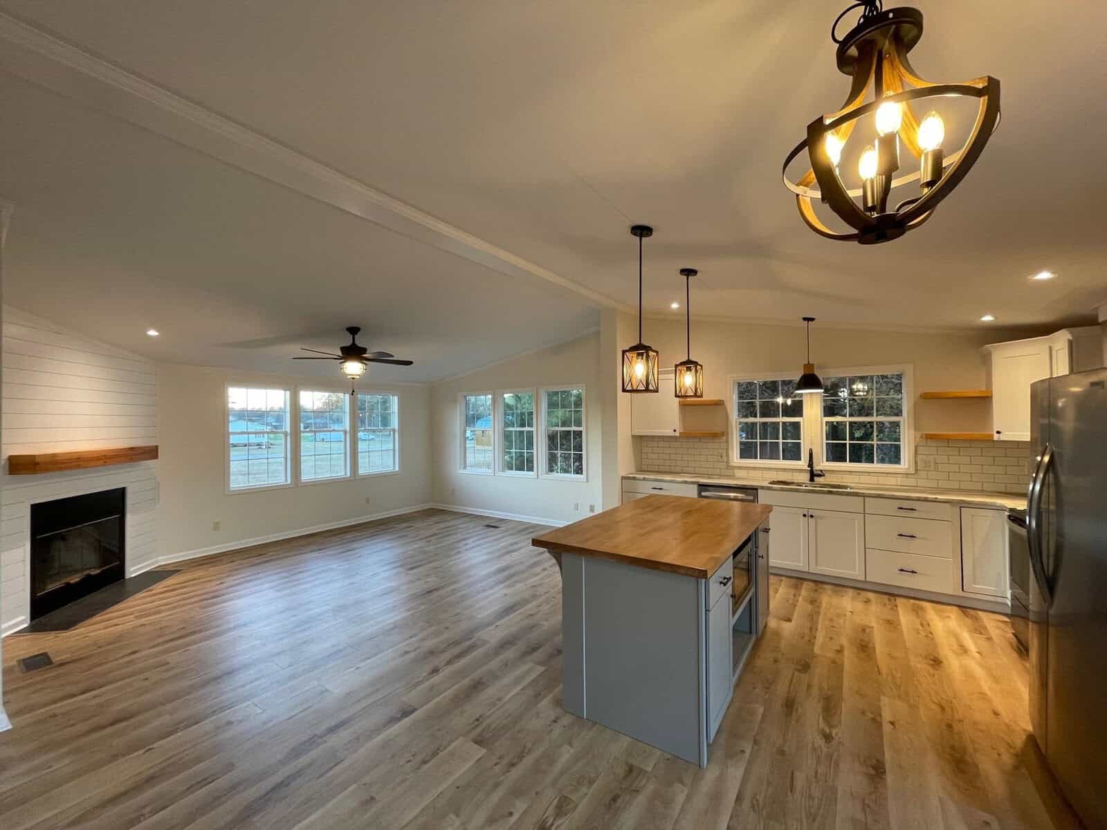 A newly renovated open-plan kitchen and living space with modern appliances, hardwood floors, white cabinetry, and stylish lighting fixtures.