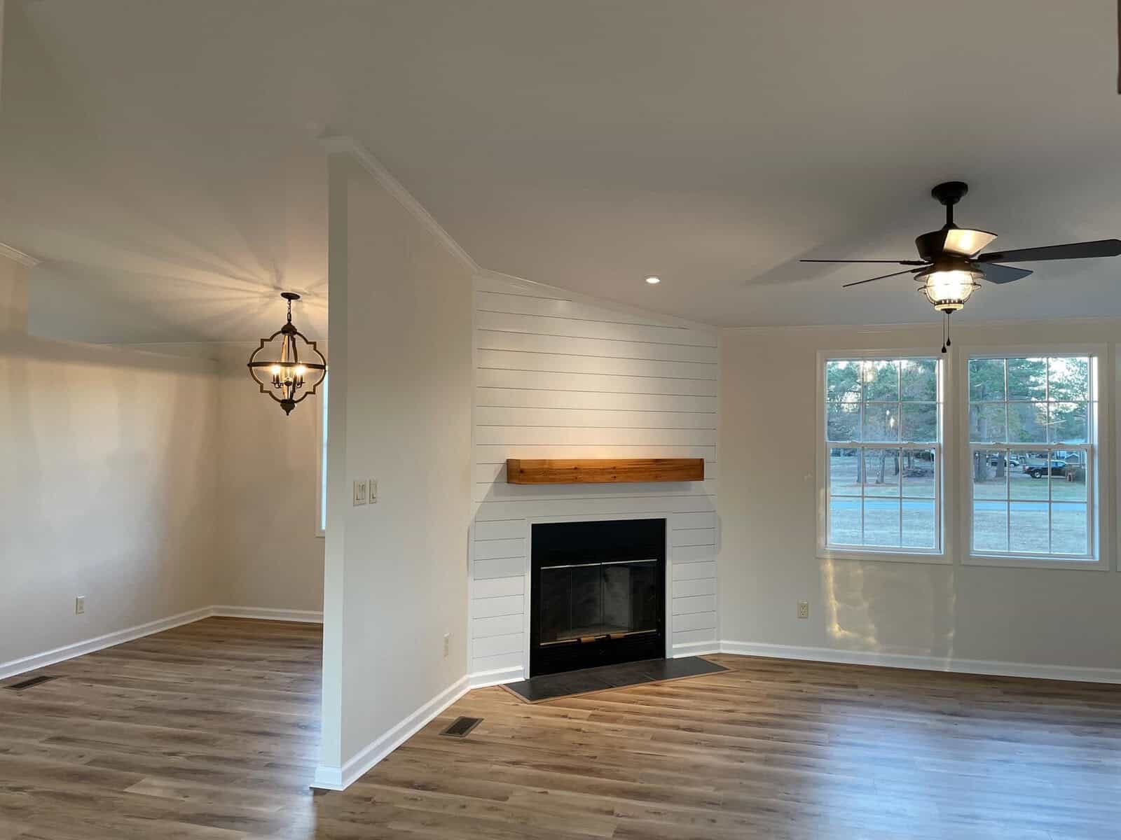 A well-lit, empty room featuring a fireplace with a white wall facade, two ceiling fans, pendant lighting, and laminate flooring.