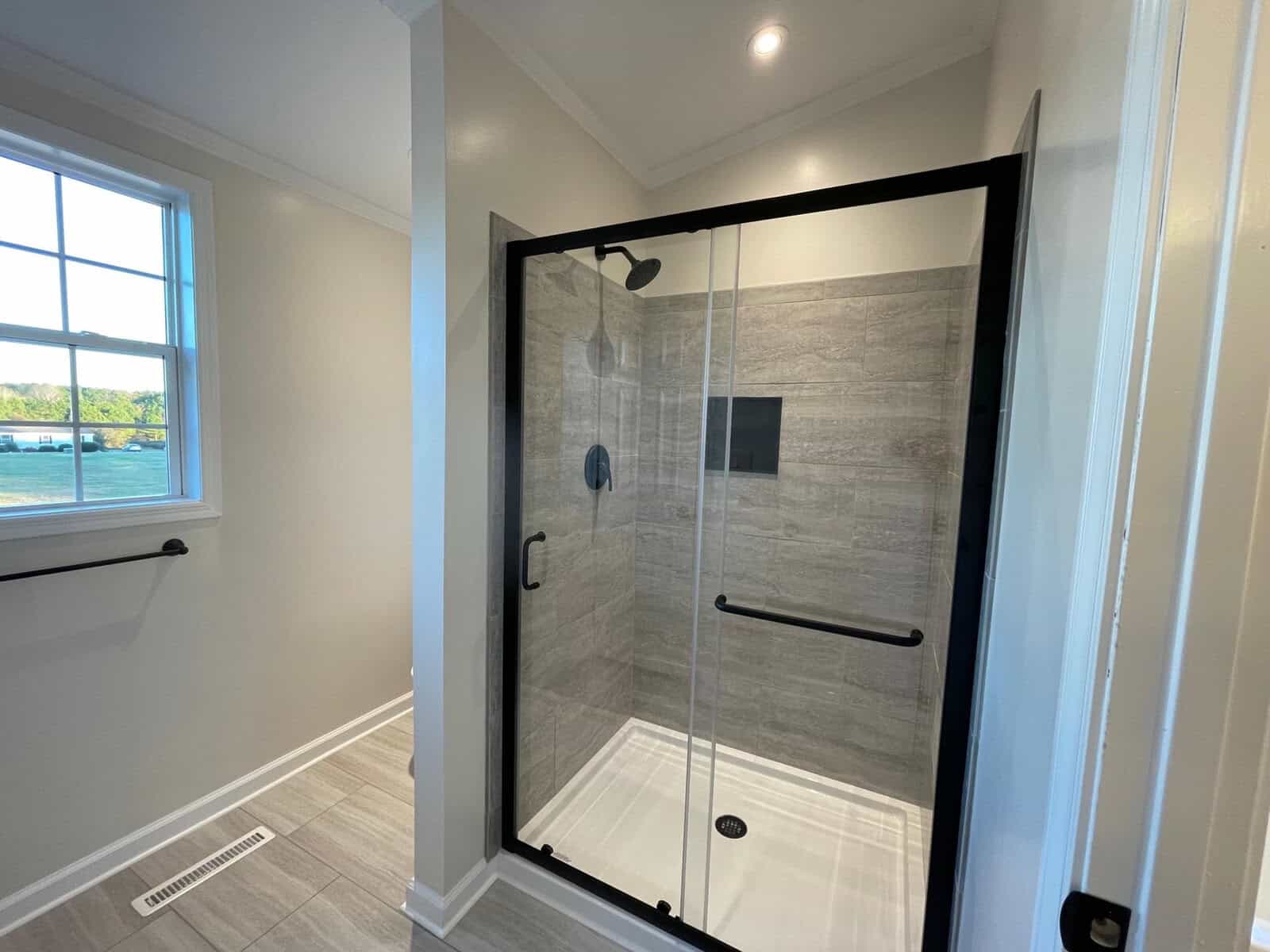 A modern bathroom featuring a walk-in shower with black frame doors and grey tiled walls.