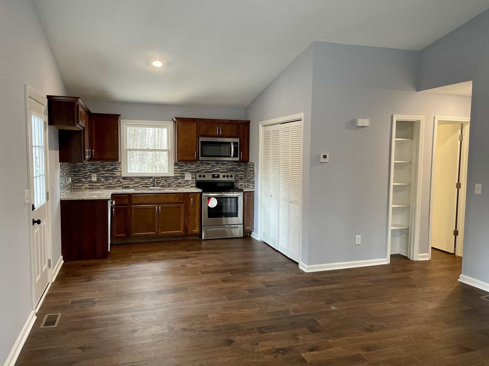 A modern kitchen with wooden flooring, stainless steel appliances, and dark brown cabinets.