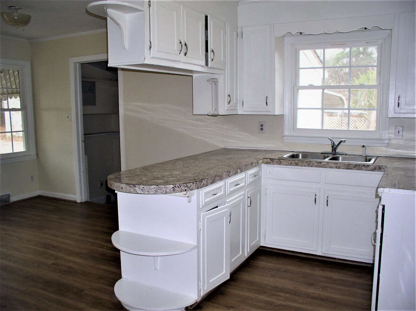 A clean and empty kitchen with white cabinets, granite countertops, and vinyl flooring.