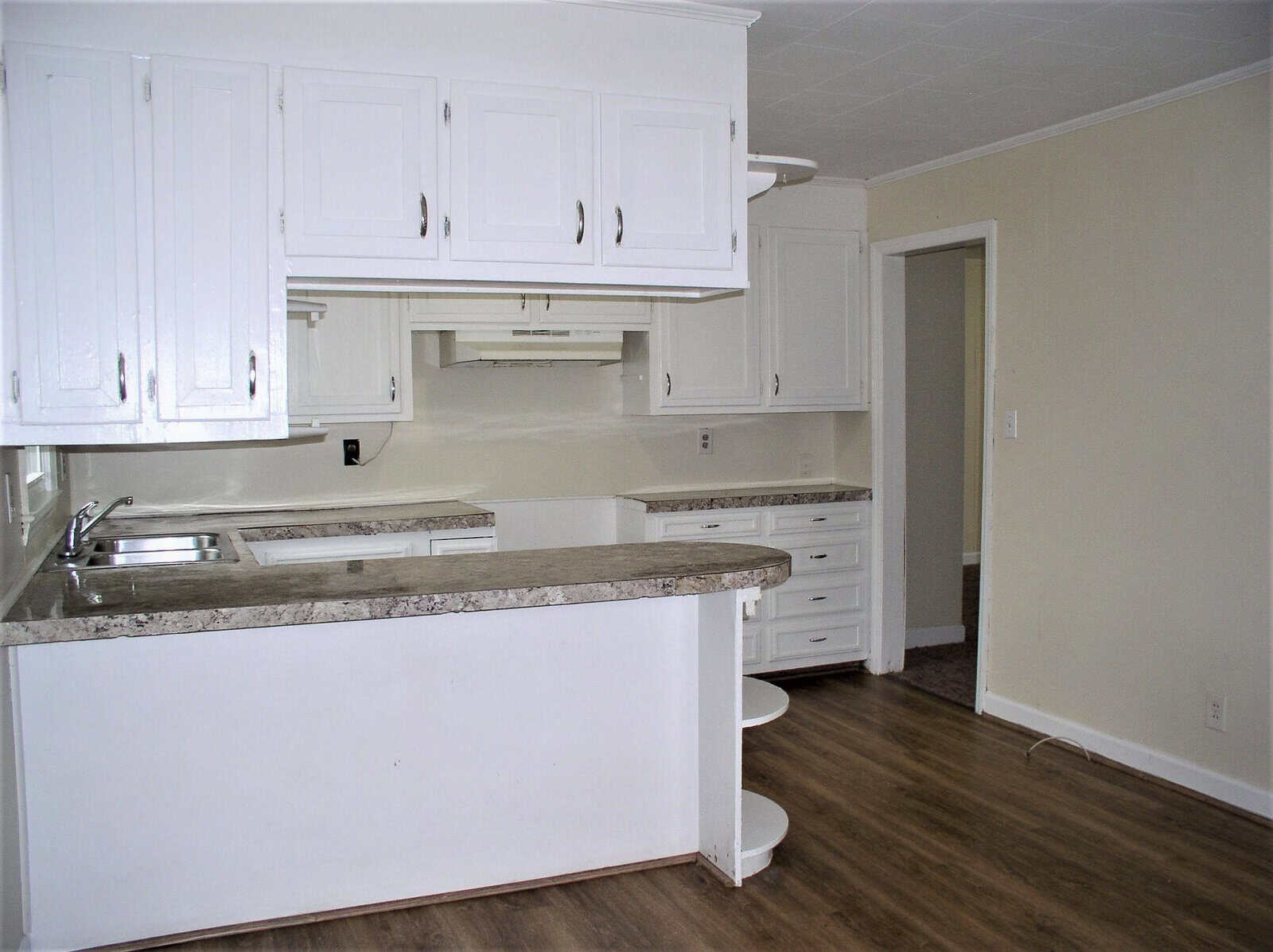 A spacious kitchen with white cabinetry, granite countertops, and dark laminate flooring, featuring a breakfast bar and an open doorway leading to an adjacent room.