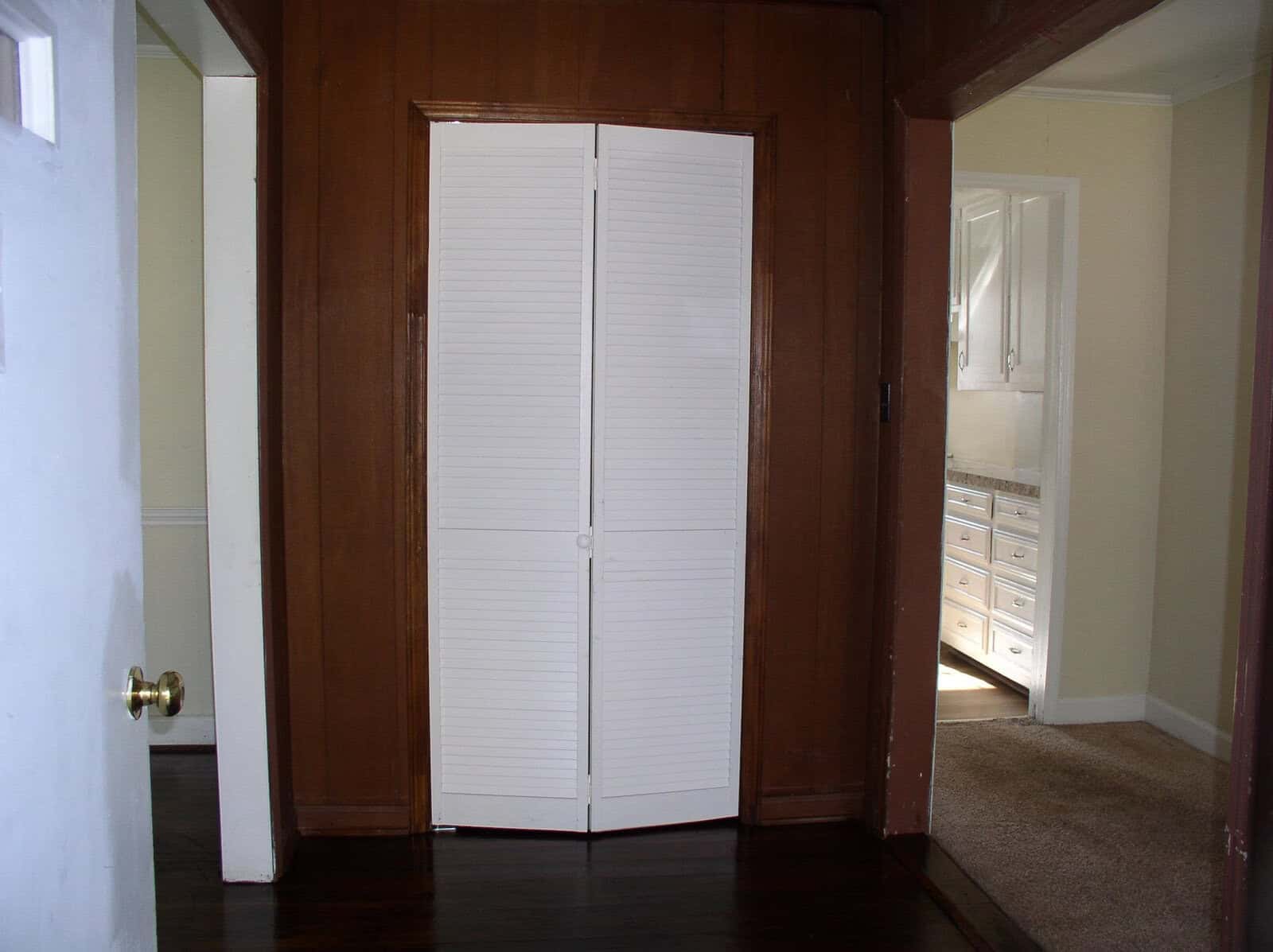 An empty room featuring a white closed closet door flanked by wooden brown walls, with a built-in chest of drawers visible in the adjacent space.