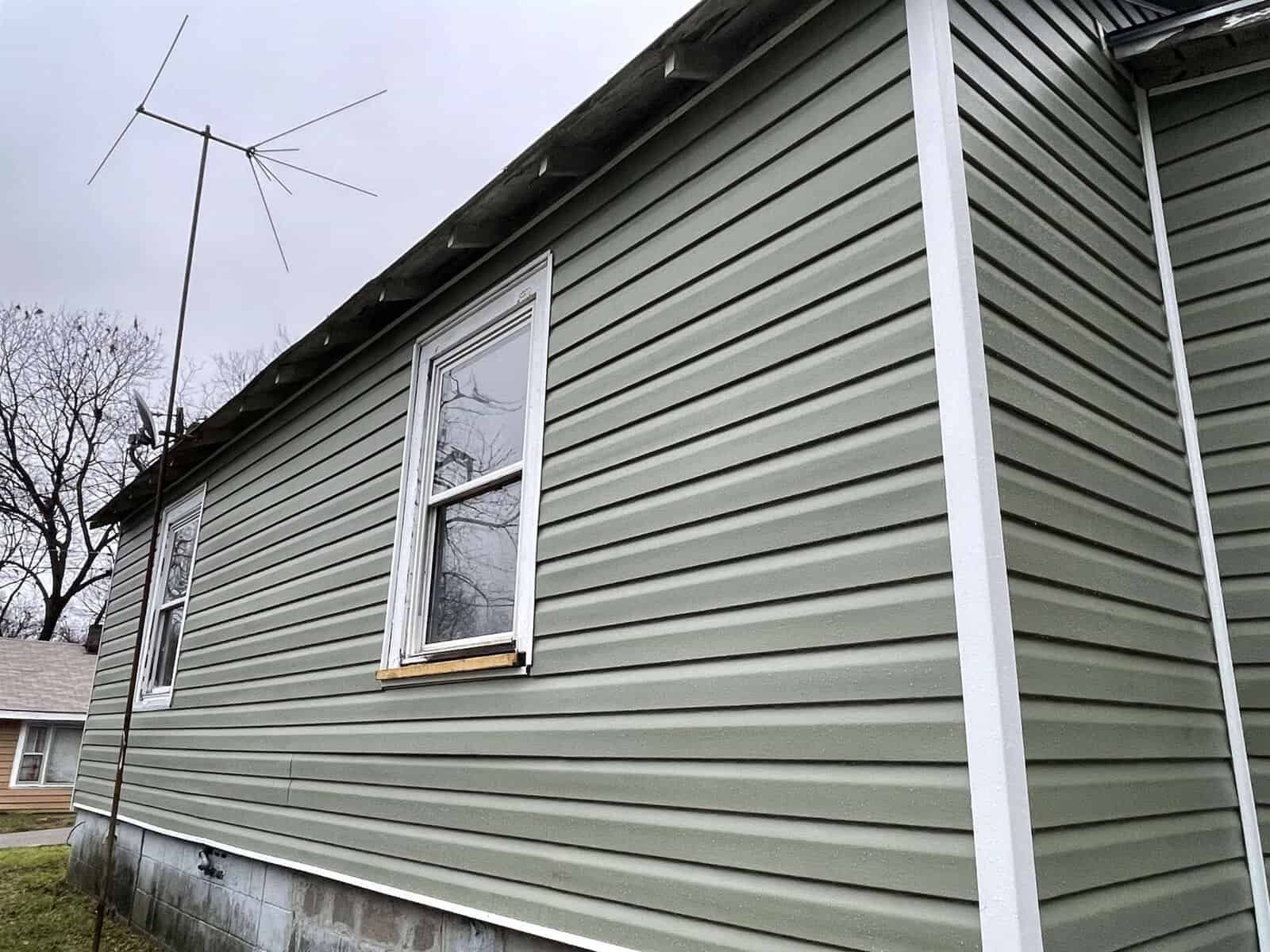 A side view of a house with green siding, featuring two windows and a rooftop tv antenna.