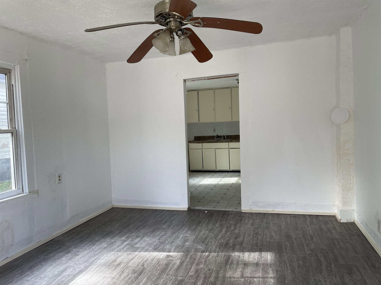 A vacant room with white walls and gray flooring, featuring a ceiling fan and an open doorway leading to an adjoining room with tiled floors.