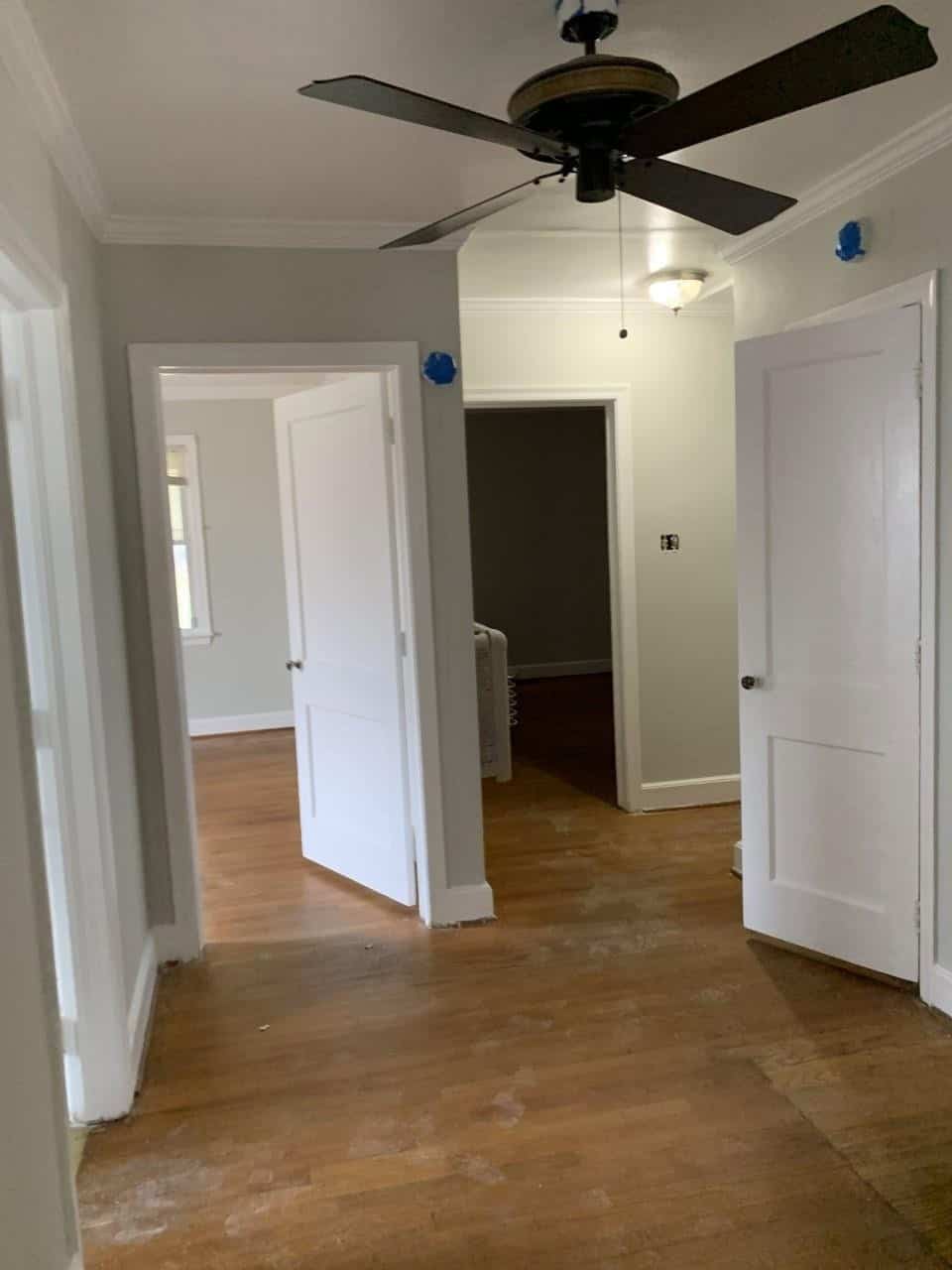 An empty room with hardwood floors featuring an open door, a closed door, and a ceiling fan.