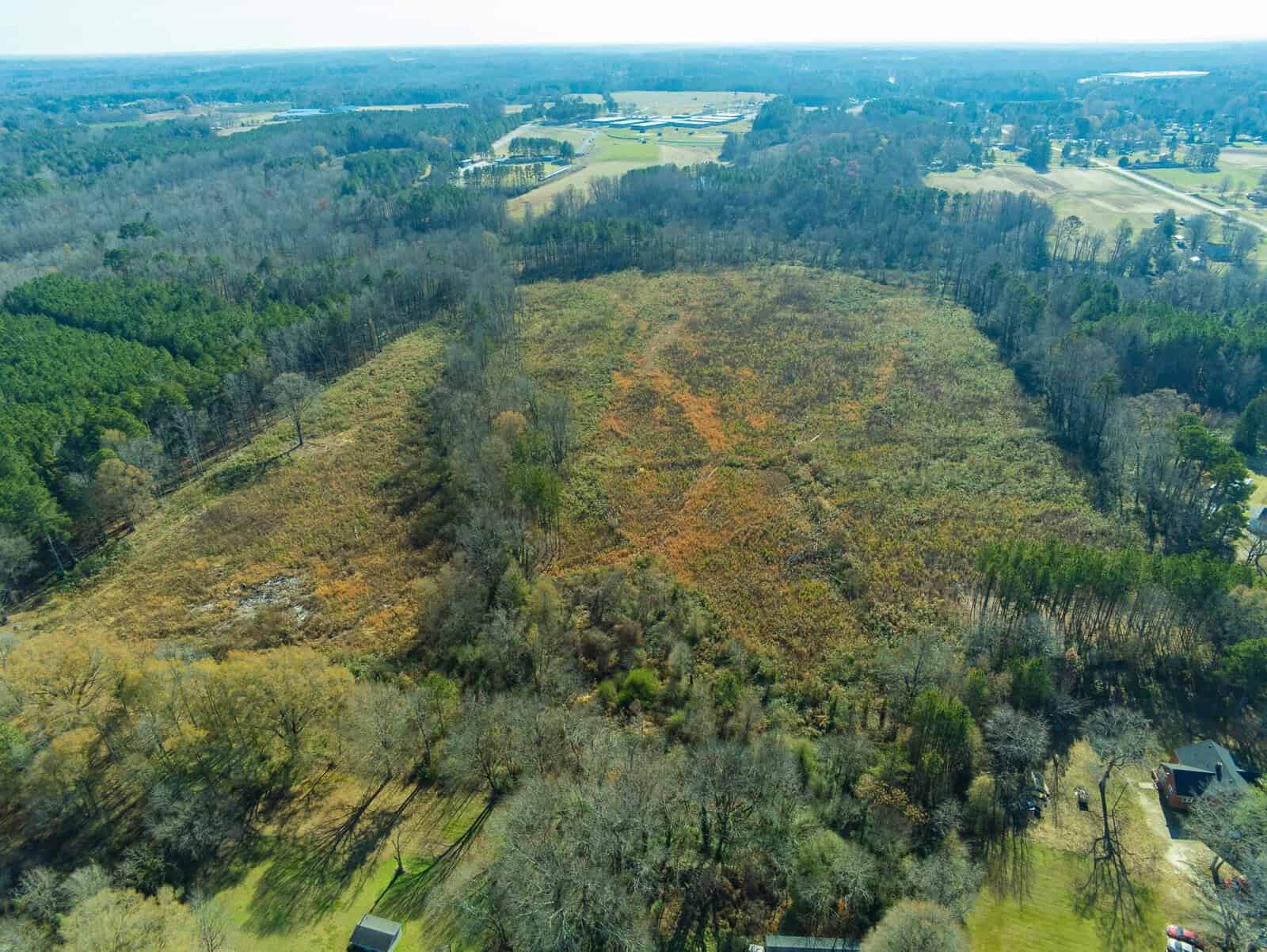 Aerial view of a mixed landscape featuring areas of dense trees, cleared land, and signs of human habitation with buildings and roads.