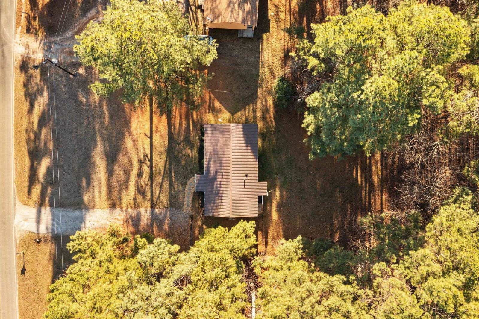 Aerial view of a solitary house surrounded by trees with a long shadow cast by the afternoon sun.