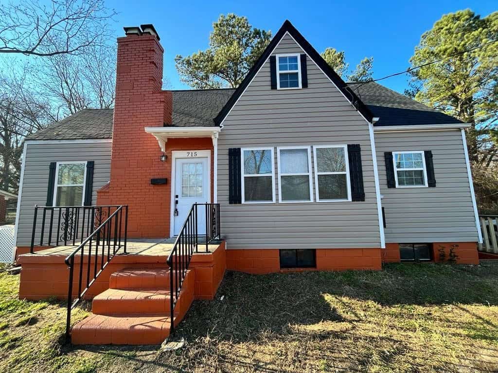 A two-story house at 715 Highland Avenue, Henderson NC, with gray siding and orange accents, featuring a red-brick chimney and staircase.