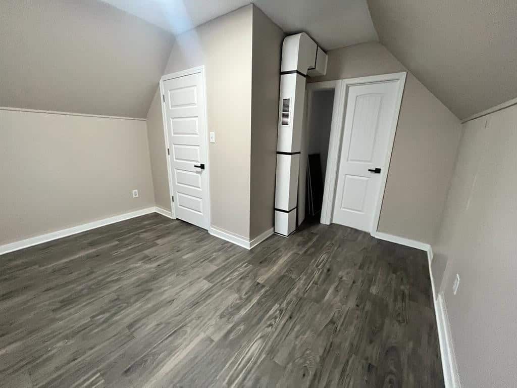An empty room with gray laminate flooring, white walls, a closed white door, and a white storage closet under a sloped ceiling.