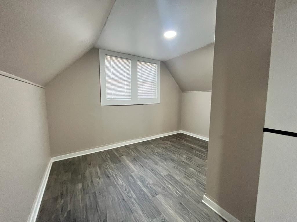 An empty room featuring slanted walls under a pitched roof with a single window and recessed lighting.