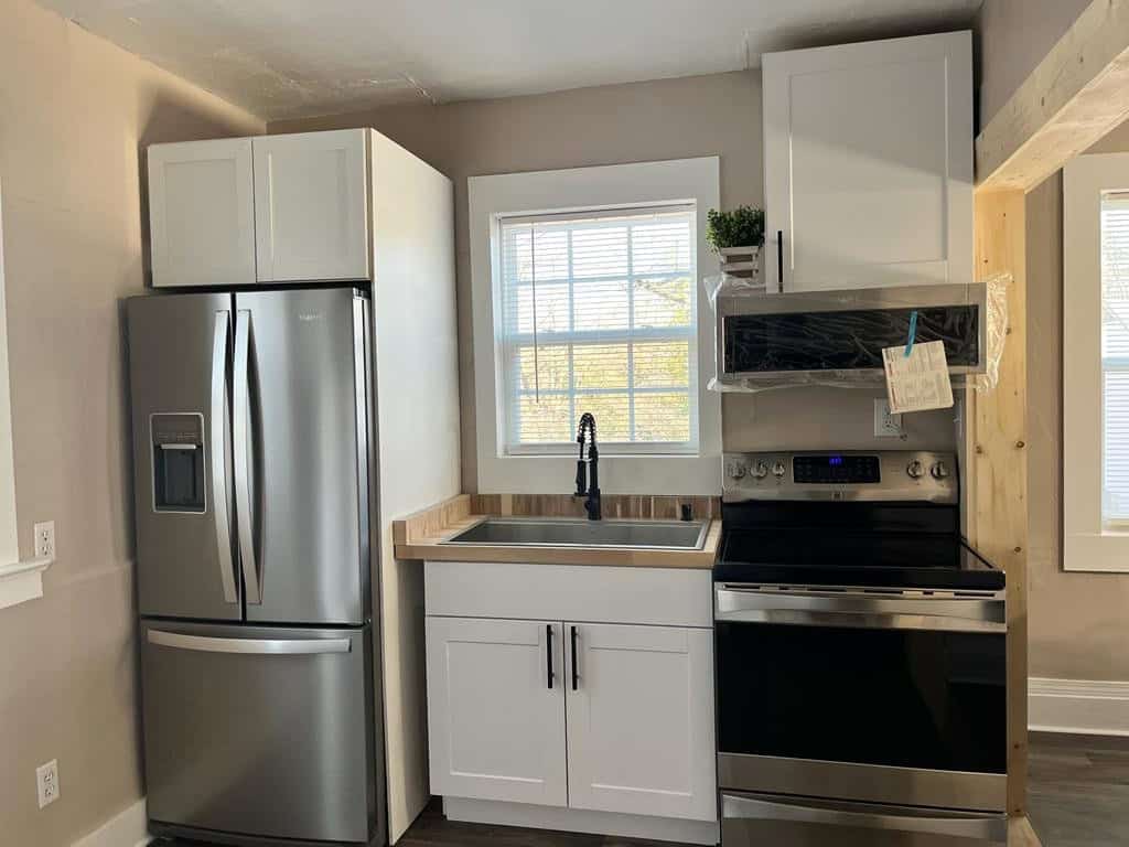 A modern kitchenette with stainless steel appliances, white cabinetry, and a wooden countertop.
