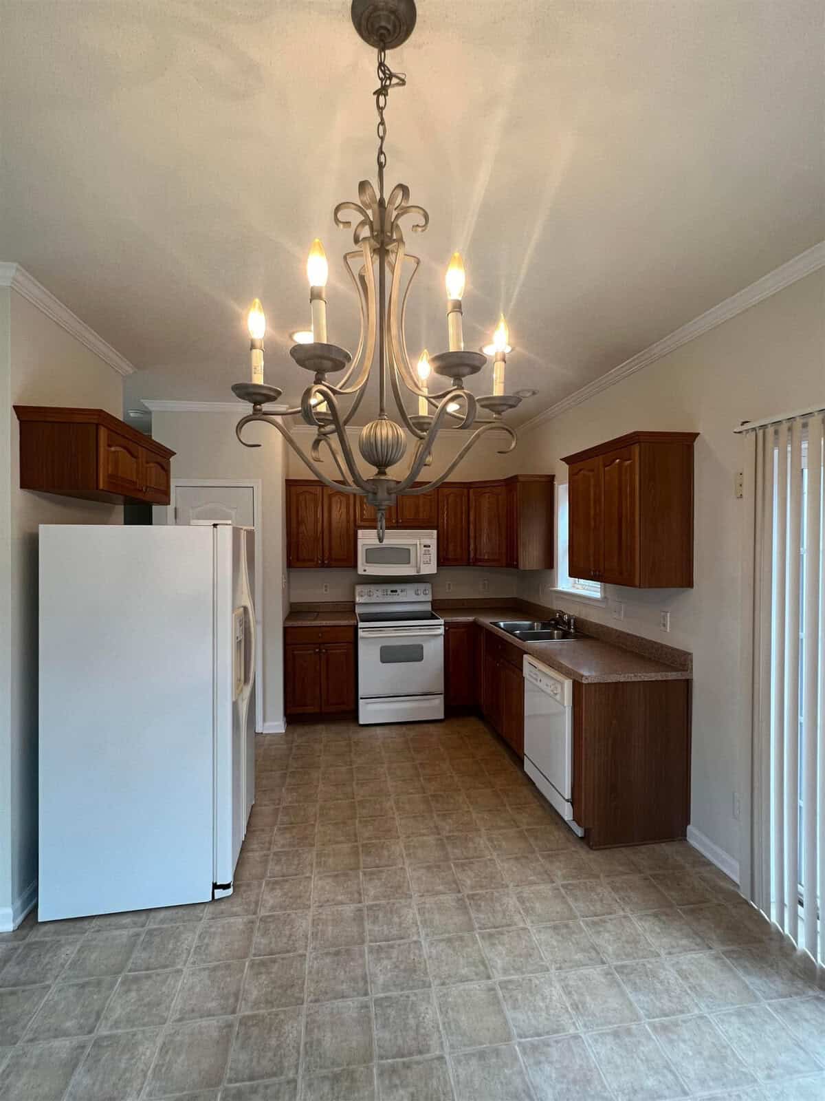 A well-lit kitchen with wooden cabinets, white appliances, and an ornate chandelier.