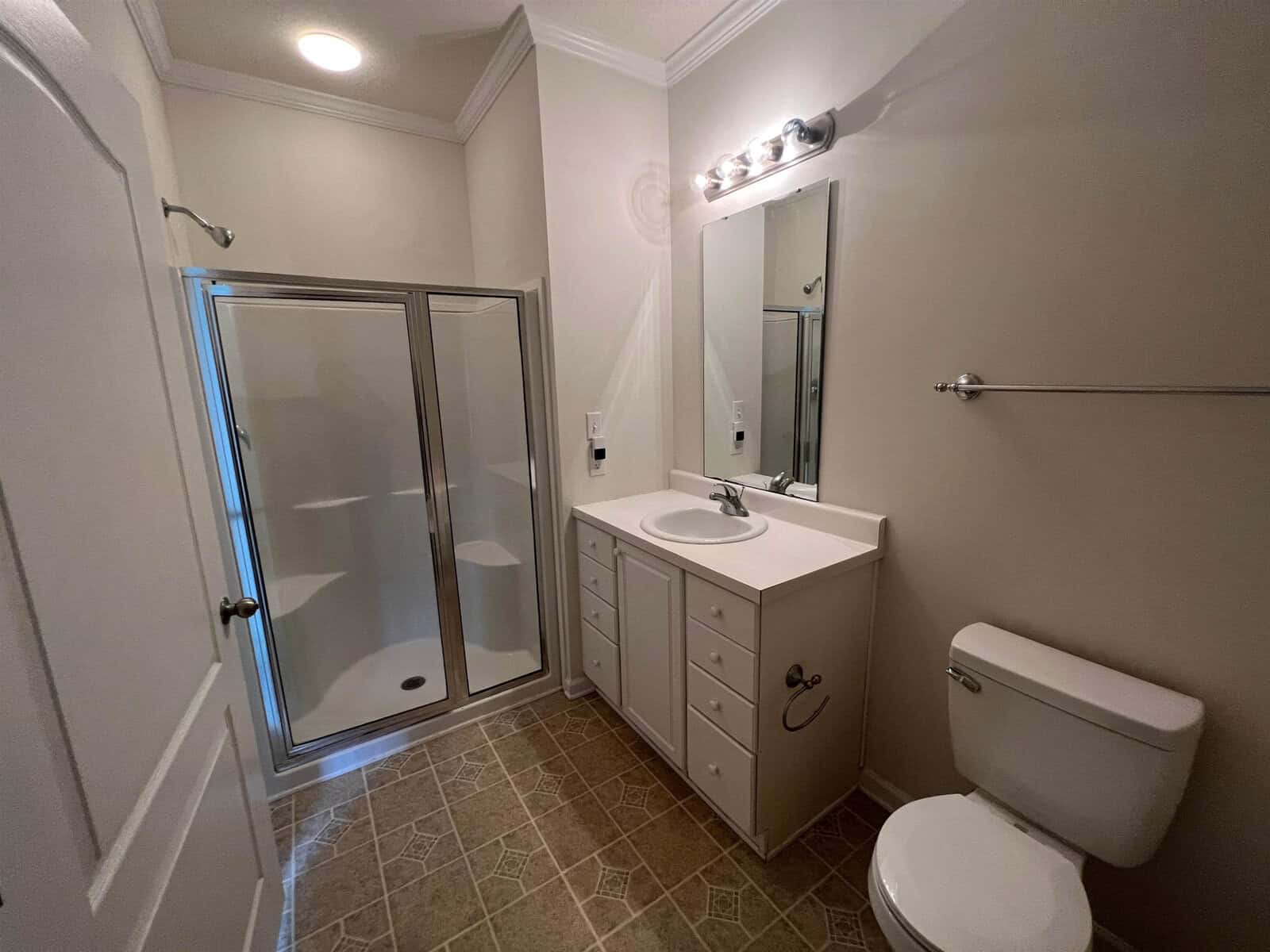 A modern bathroom with a shower cabin, a vanity with a sink, a wall-mounted mirror, light fixtures, and a toilet.