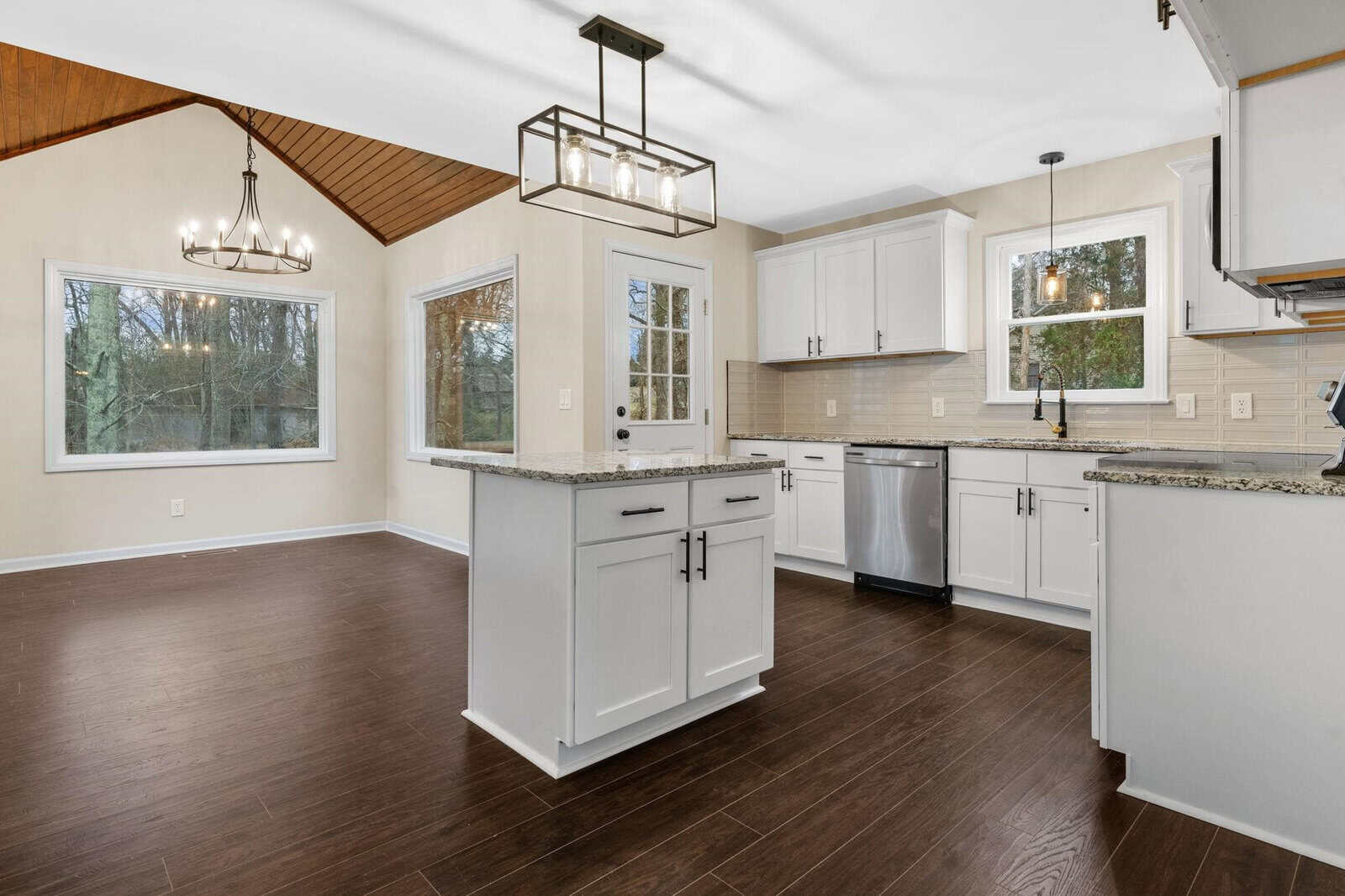 A modern kitchen with white cabinets, dark wood flooring, and stainless steel appliances, featuring a central island and pendant lighting.