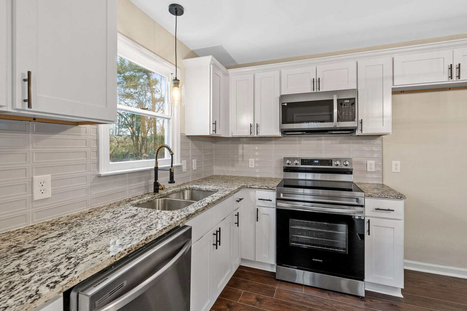 A modern kitchen with stainless steel appliances, white cabinetry, granite countertops, and a tile backsplash.