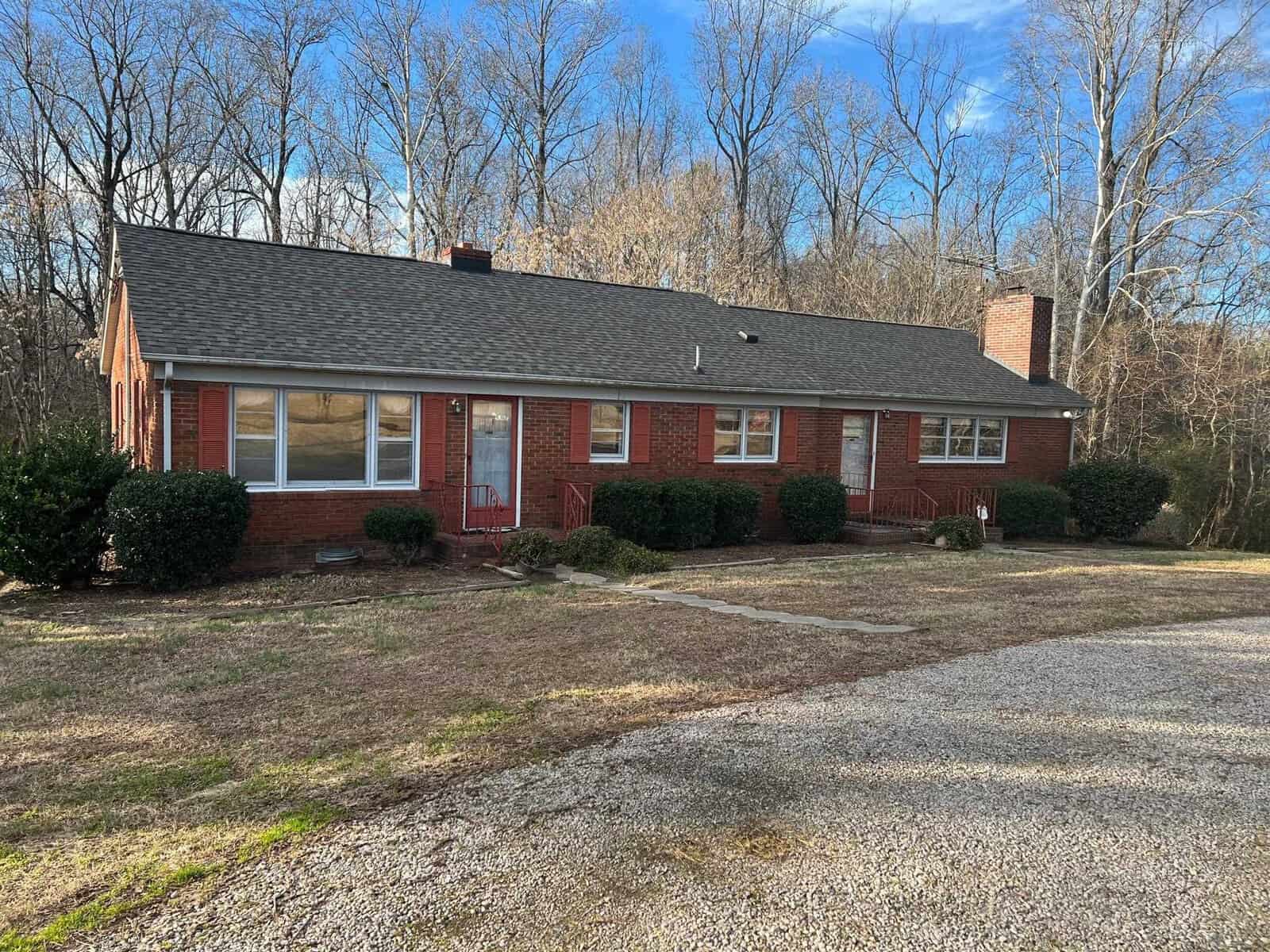 A single-story red brick house with white-trimmed windows, a shingled roof, and a chimney at 933 Daniel Harris Road, Henderson NC, surrounded by bare trees and a lawn with