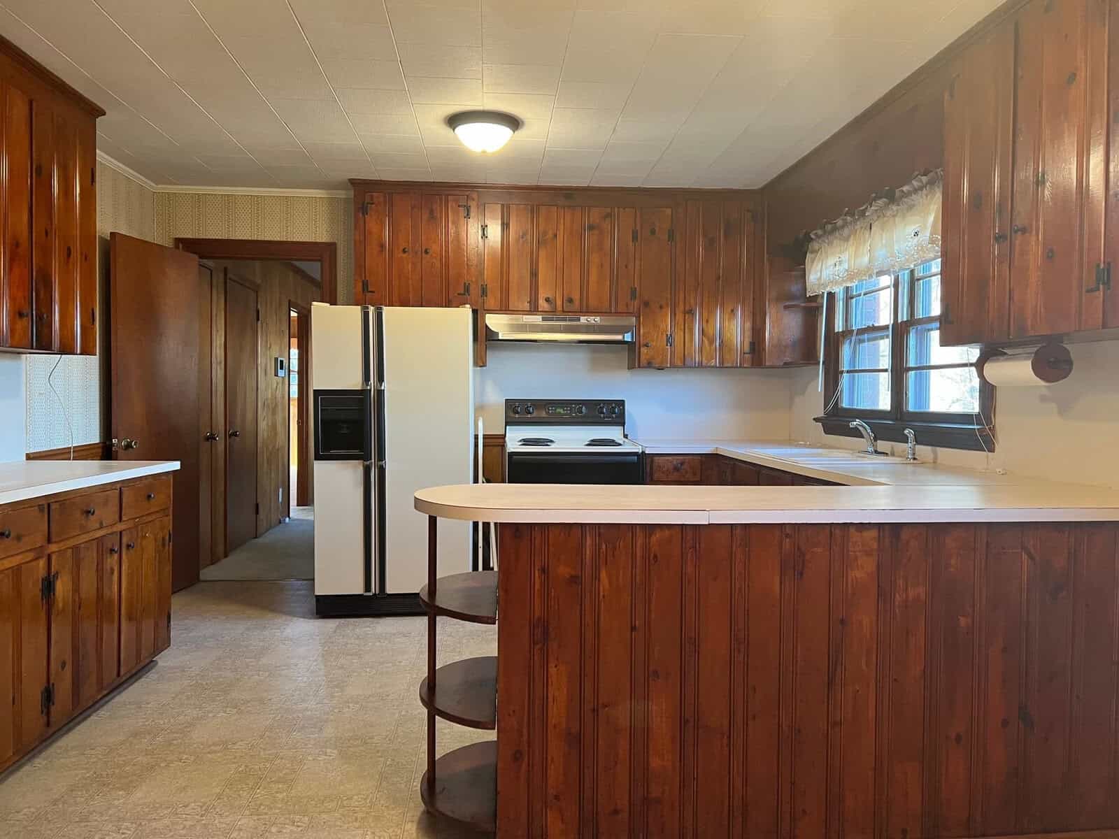 A kitchen with wooden cabinetry, white appliances, and a bar-height counter with stools.