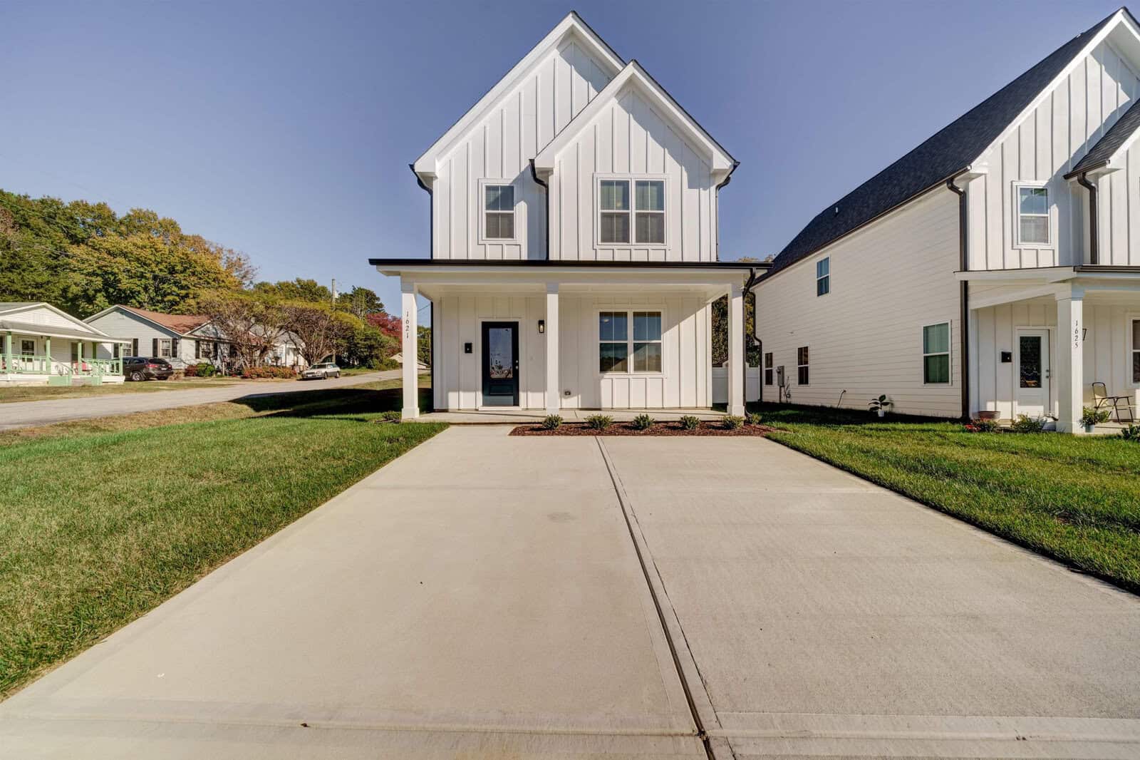 A modern two-story house featuring a white exterior with a black roof, concrete driveway, and a small front yard, situated in a residential neighborhood.