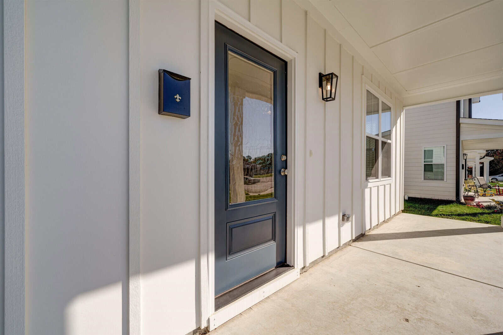 A residential front porch with a blue front door featuring a glass panel and a decorative star, viewed on a sunny day.