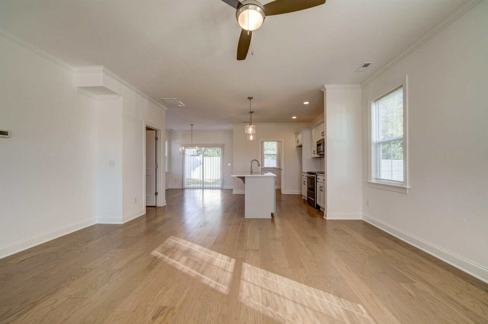 An empty, open-concept living space with hardwood floors, white walls, and natural light coming in through the windows.