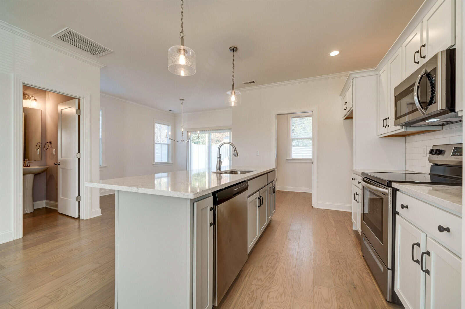A modern kitchen with white cabinetry, stainless steel appliances, and a central island under pendant lighting, leading into an adjacent room with a arched doorway.