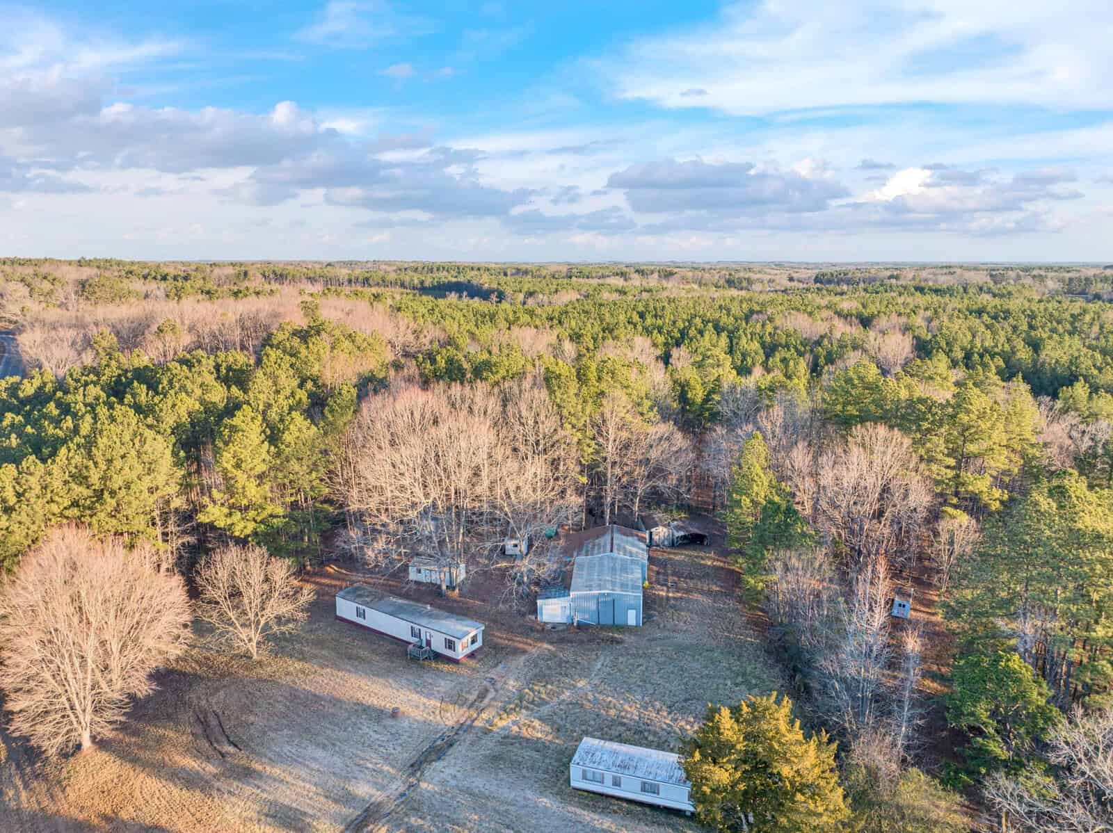 Aerial view of a rural landscape with two mobile homes and a fenced area among a wooded terrain.