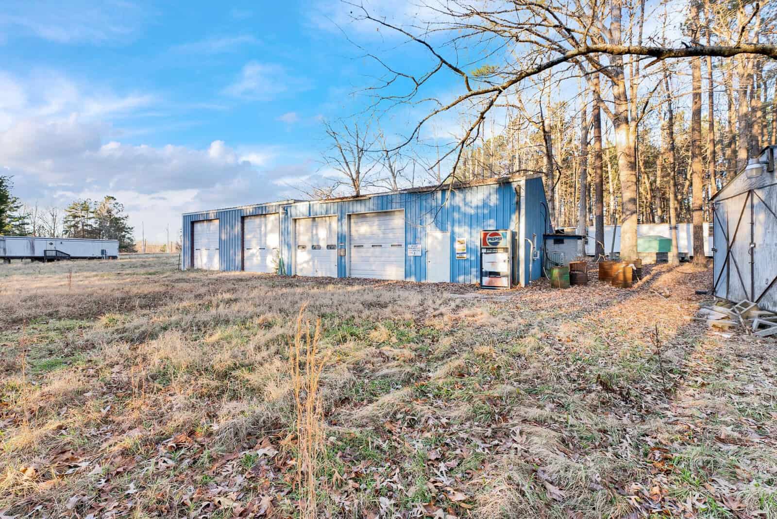 A large, blue industrial-style building with multiple garage doors set in a field with bare trees and a clear sky in the background.