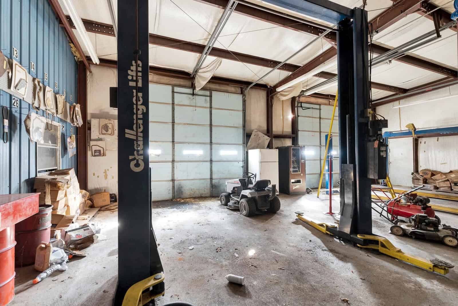 An empty automotive workshop with vehicle lifts, disused equipment, and clutter scattered across the floor.