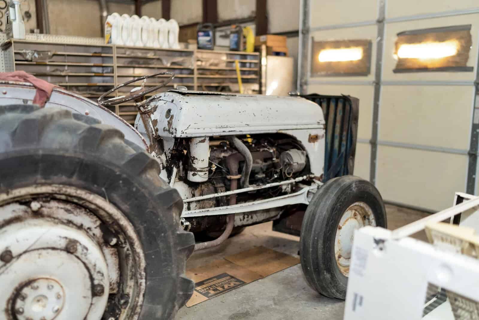 An old white tractor with worn paint and rust spots is parked inside a garage, suggesting it may be awaiting maintenance or repair.
