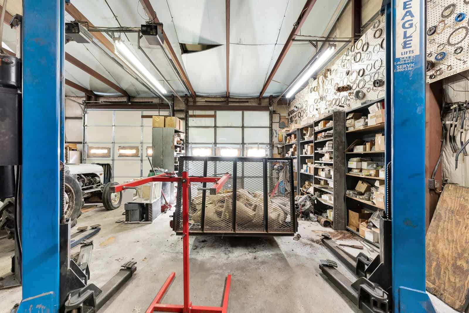 A spacious automotive workshop with a car lift, workbench, shelves with various parts, and a vehicle under repair.
