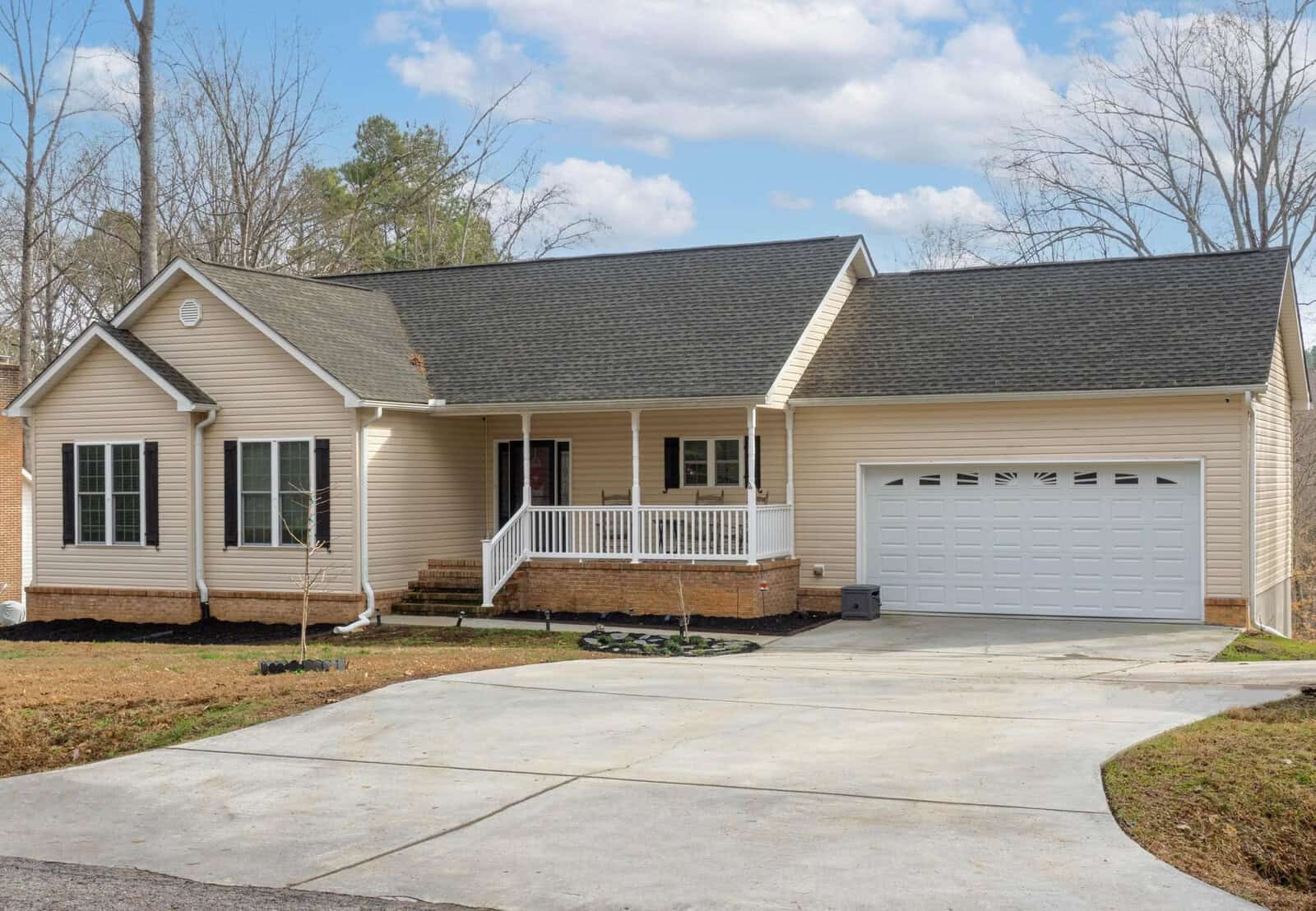 A single-story house with a white exterior, attached two-car garage, and a front porch under a clear sky.