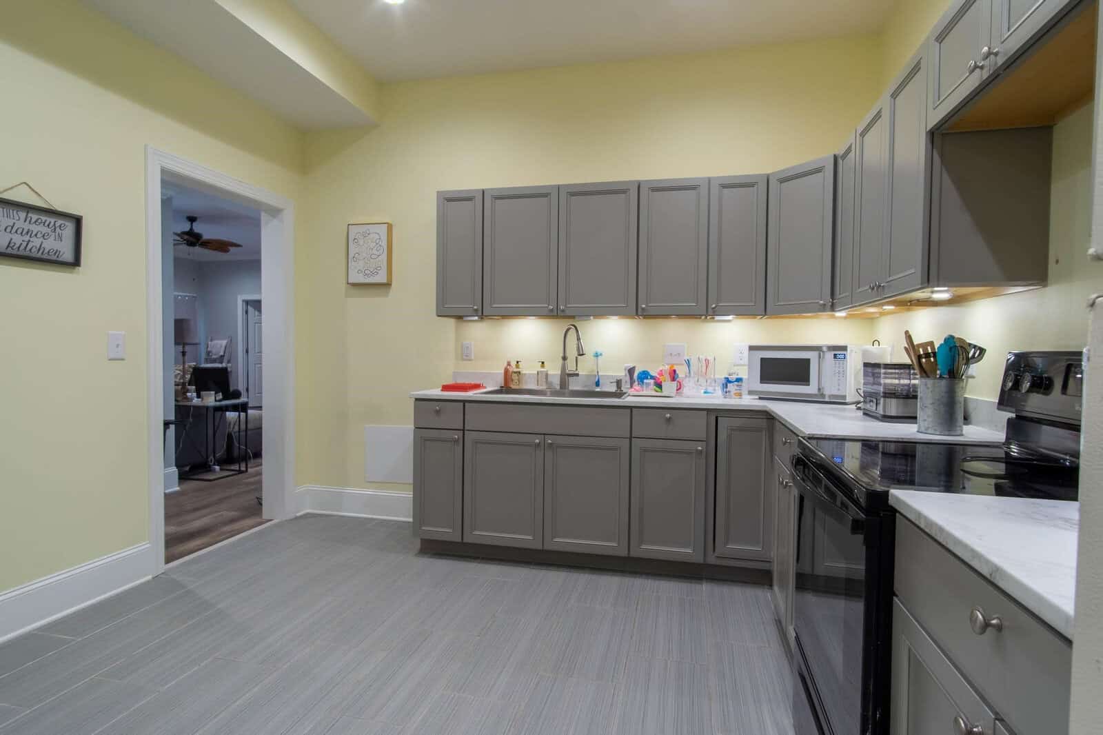 A modern kitchen with gray cabinetry, white countertops, and various appliances on the counters under artificial lighting.