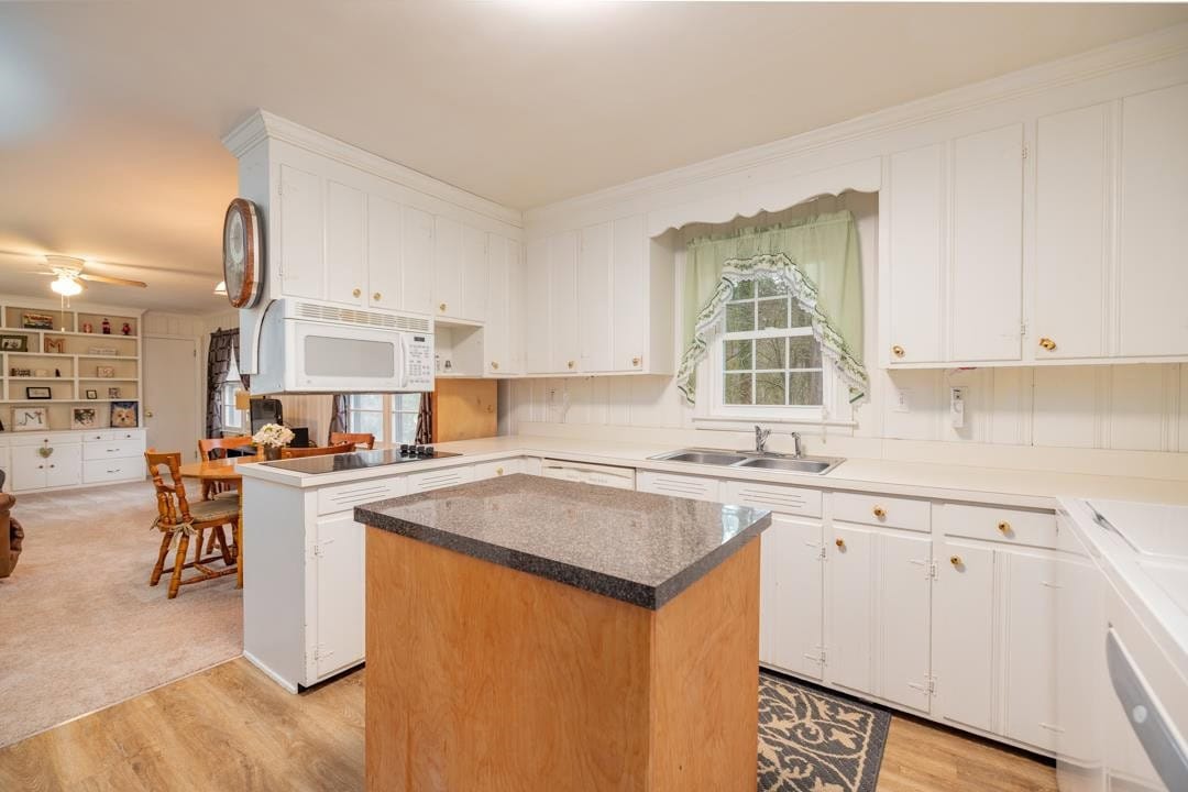A spacious kitchen with white cabinetry, black countertop, and hardwood flooring.