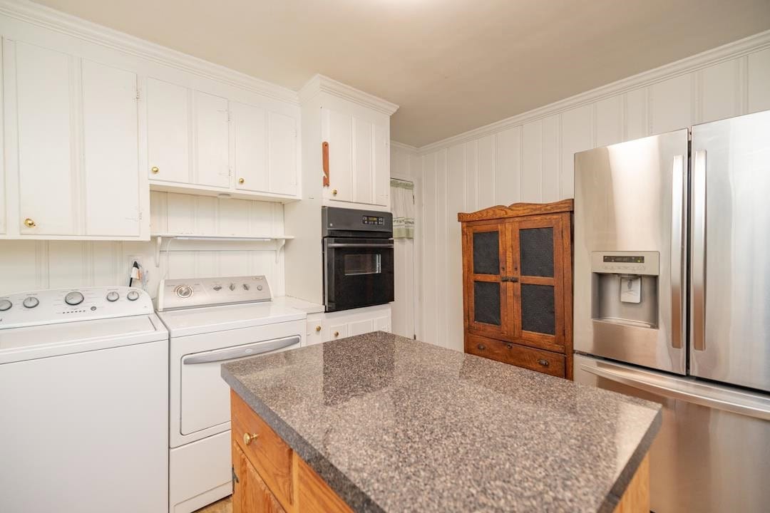 A modern kitchen interior featuring white cabinetry, stainless steel appliances, a stone countertop, and a wooden cabinet with glass panes.