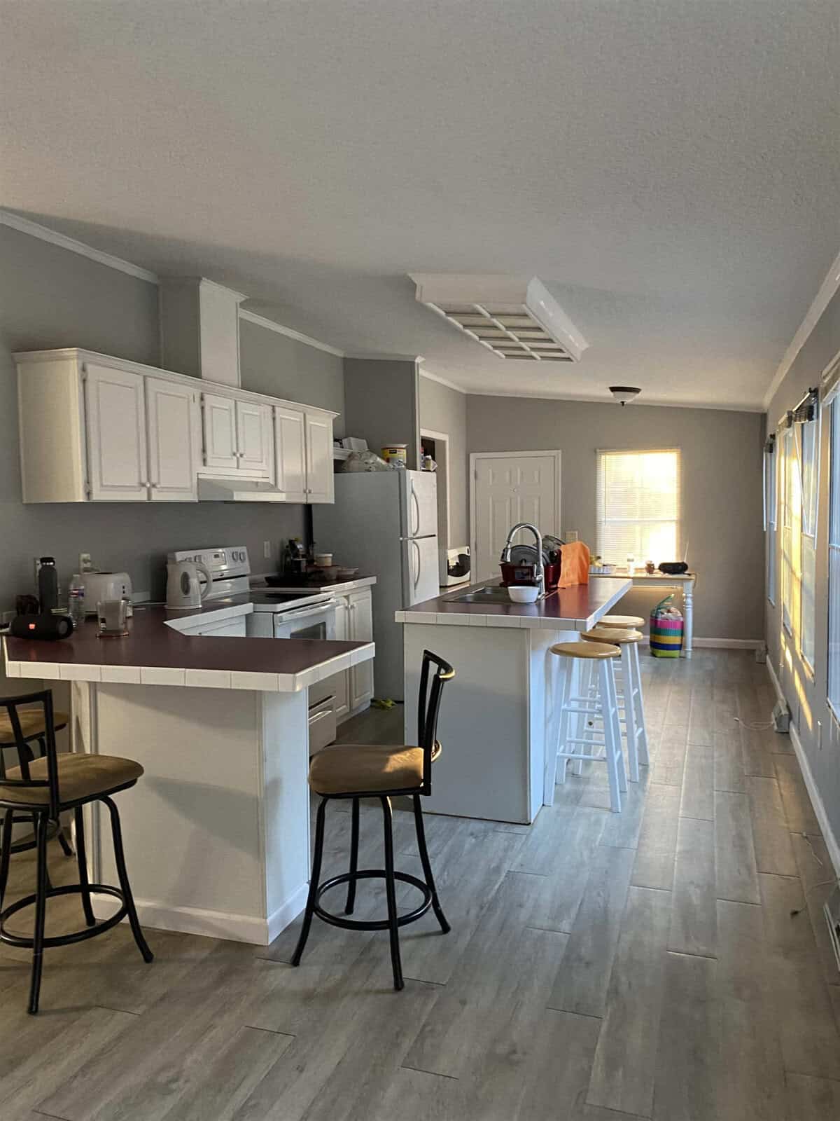 A neat kitchen with white cabinetry, modern appliances, and a breakfast bar illuminated by natural light from adjacent windows.