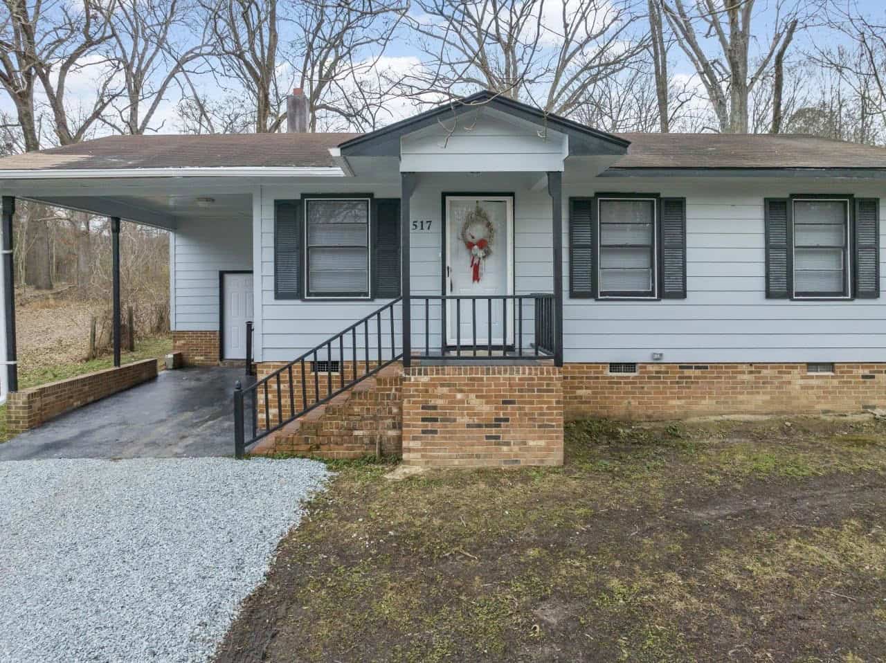 Single-story house with gray siding and white trim, located at 517 Neathery Street, Henderson NC, featuring a front porch with a wreath on the door, a carport to the left