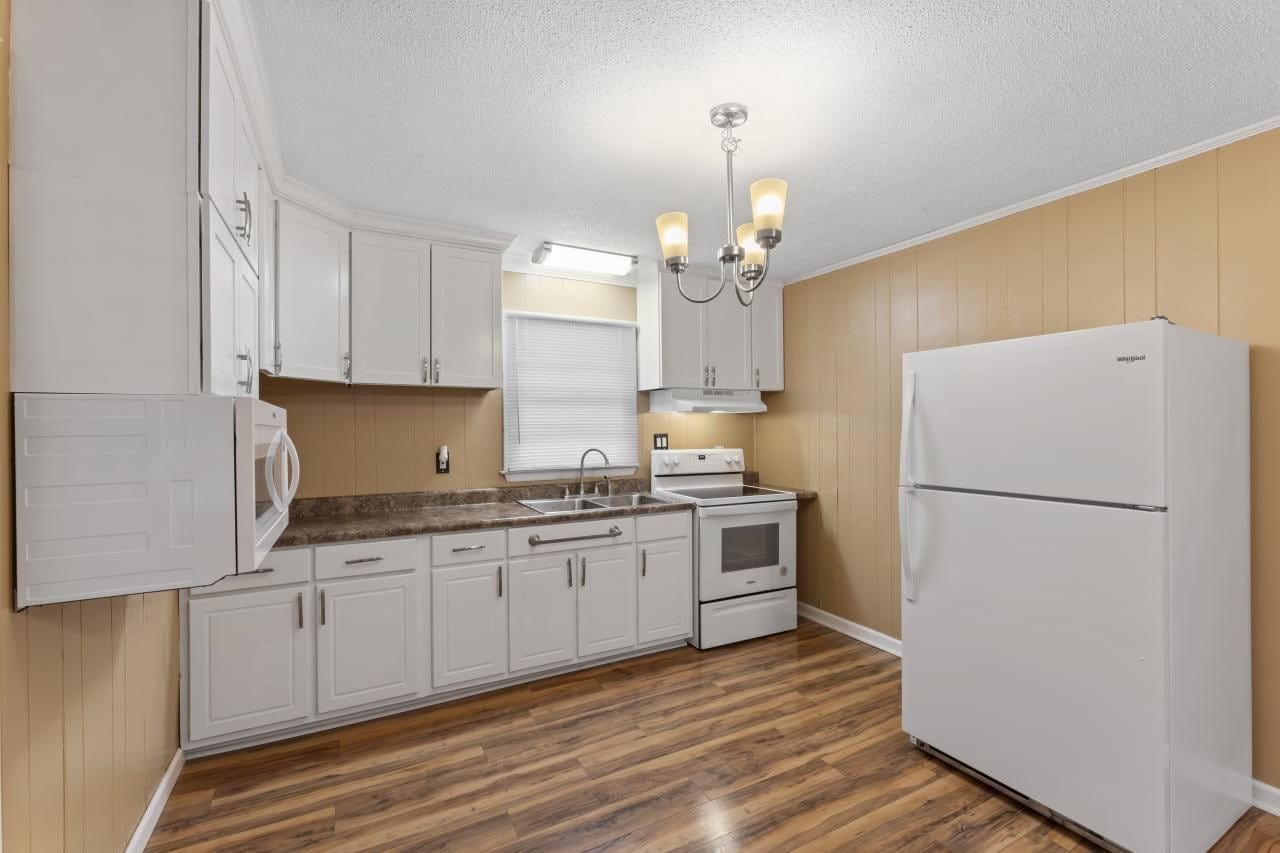 A well-lit kitchen featuring white cabinetry, granite countertops, a double-basin sink, a white refrigerator, an electric range, and wood laminate flooring.