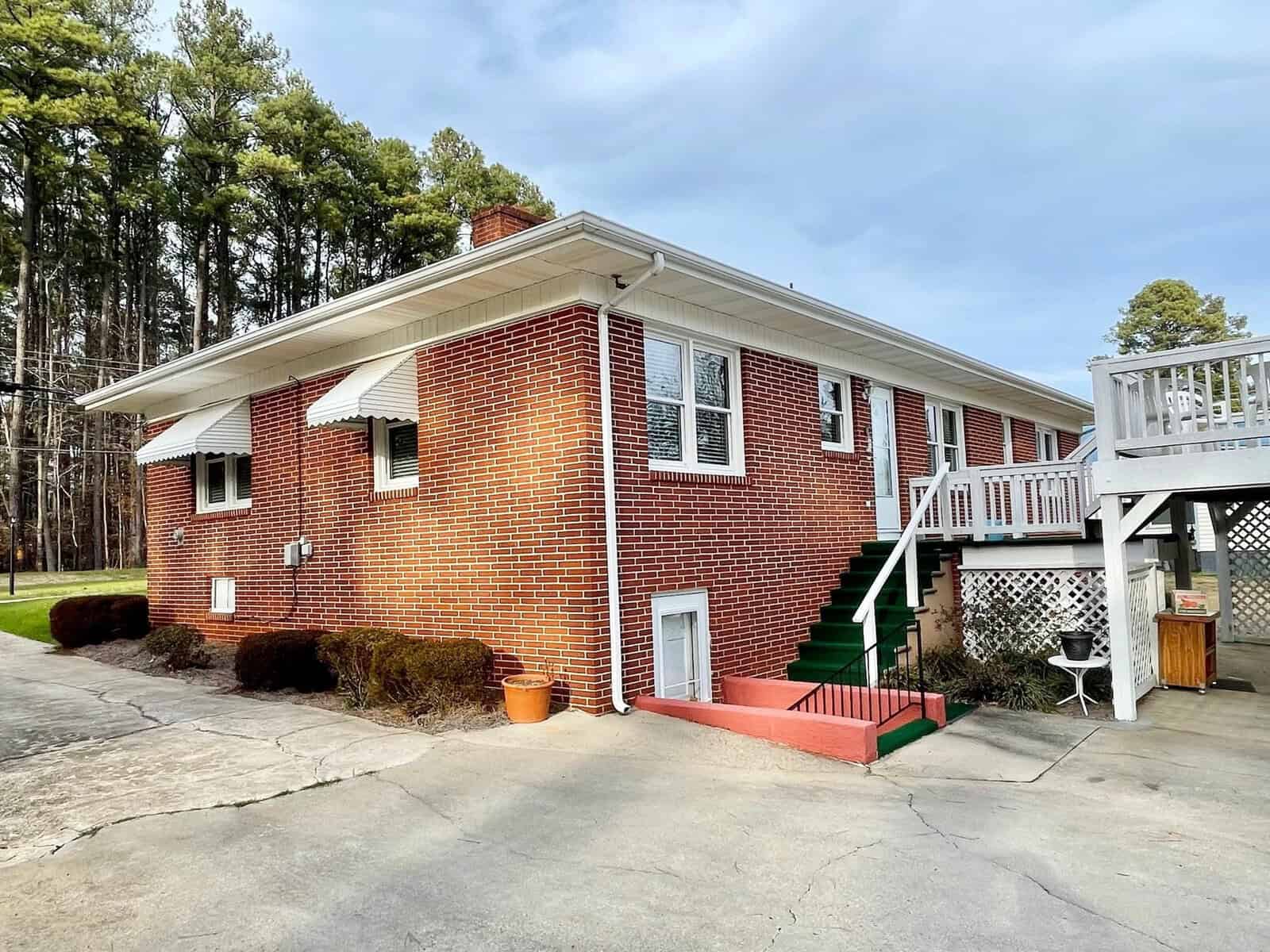 A brick single-family home with white trim and a green staircase leading to an elevated back deck.