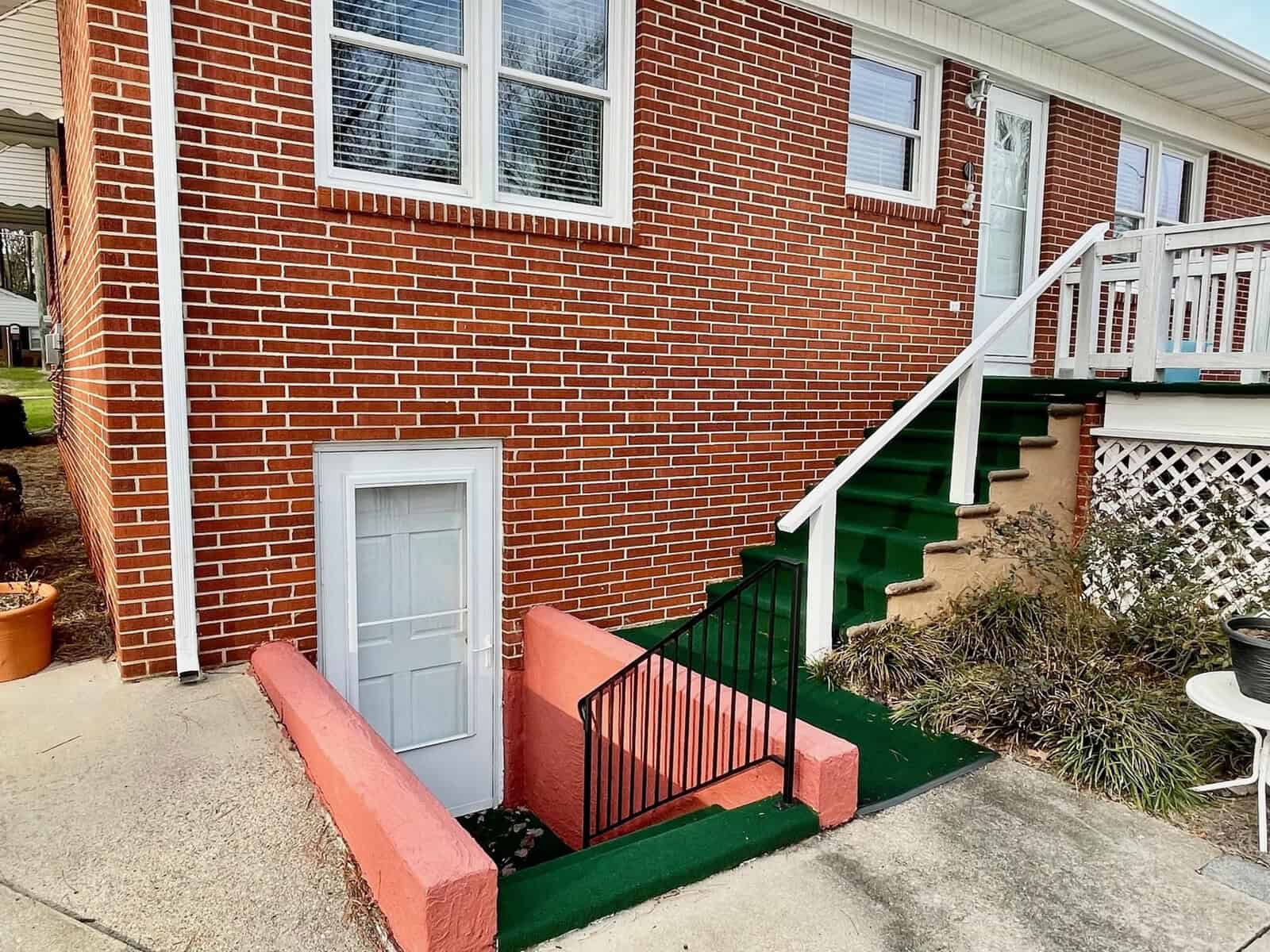 A red brick house with a white door at the base of the stairs and a set of green steps leading to a separate entrance.