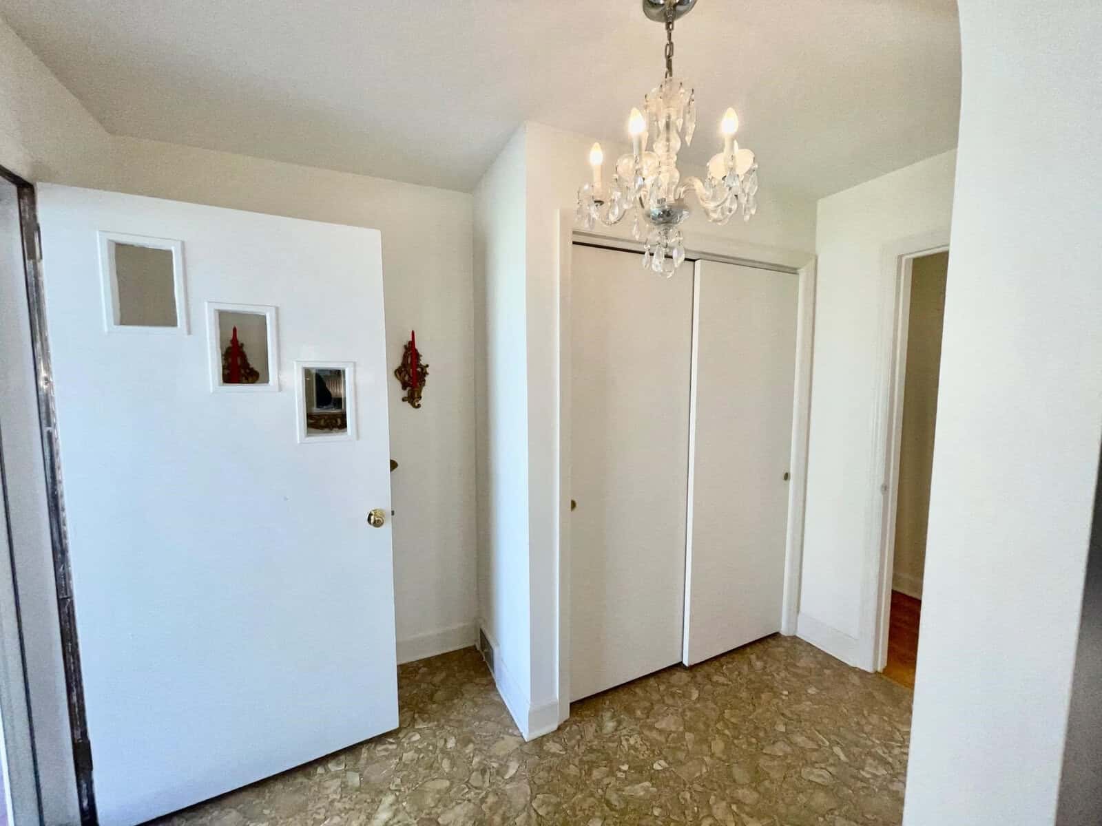 Entryway of a home featuring a white door, crystal chandelier, closed white closet doors, and a marble-patterned tile floor.