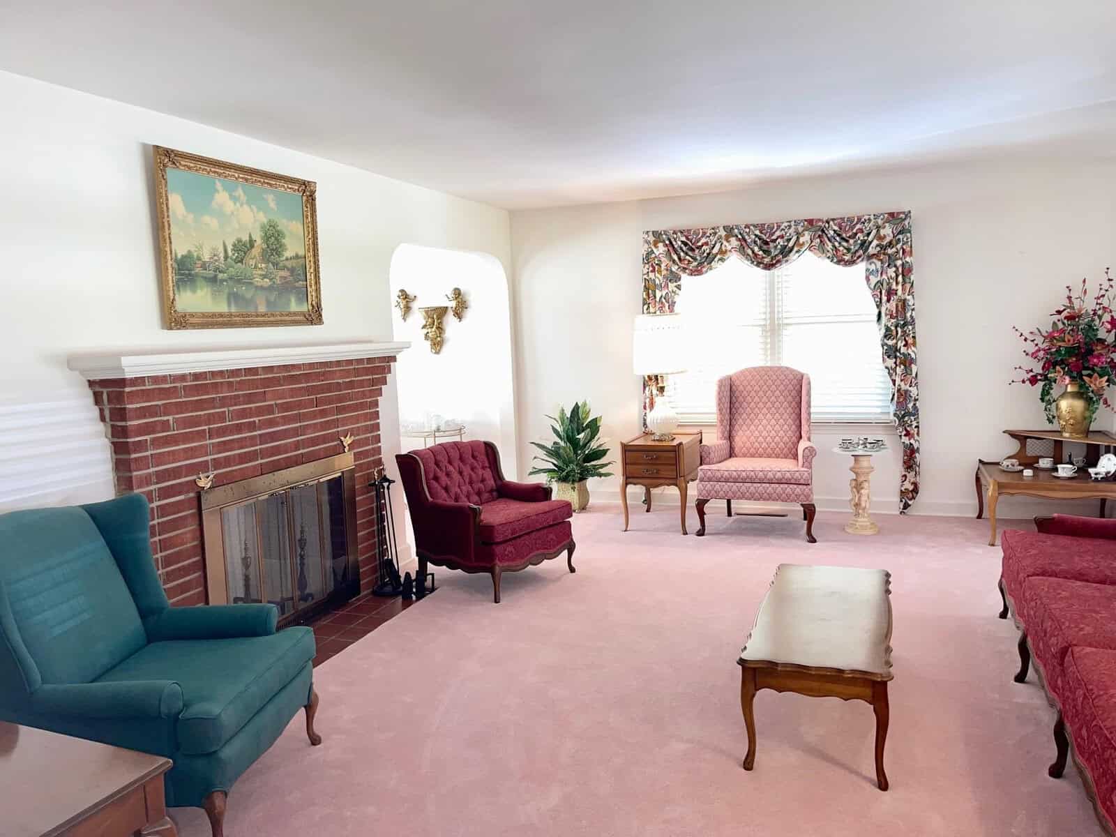 A traditional living room with a pink carpet, featuring a red brick fireplace, a variety of armchairs in different colors, wood furniture, house plants, and wall decorations.